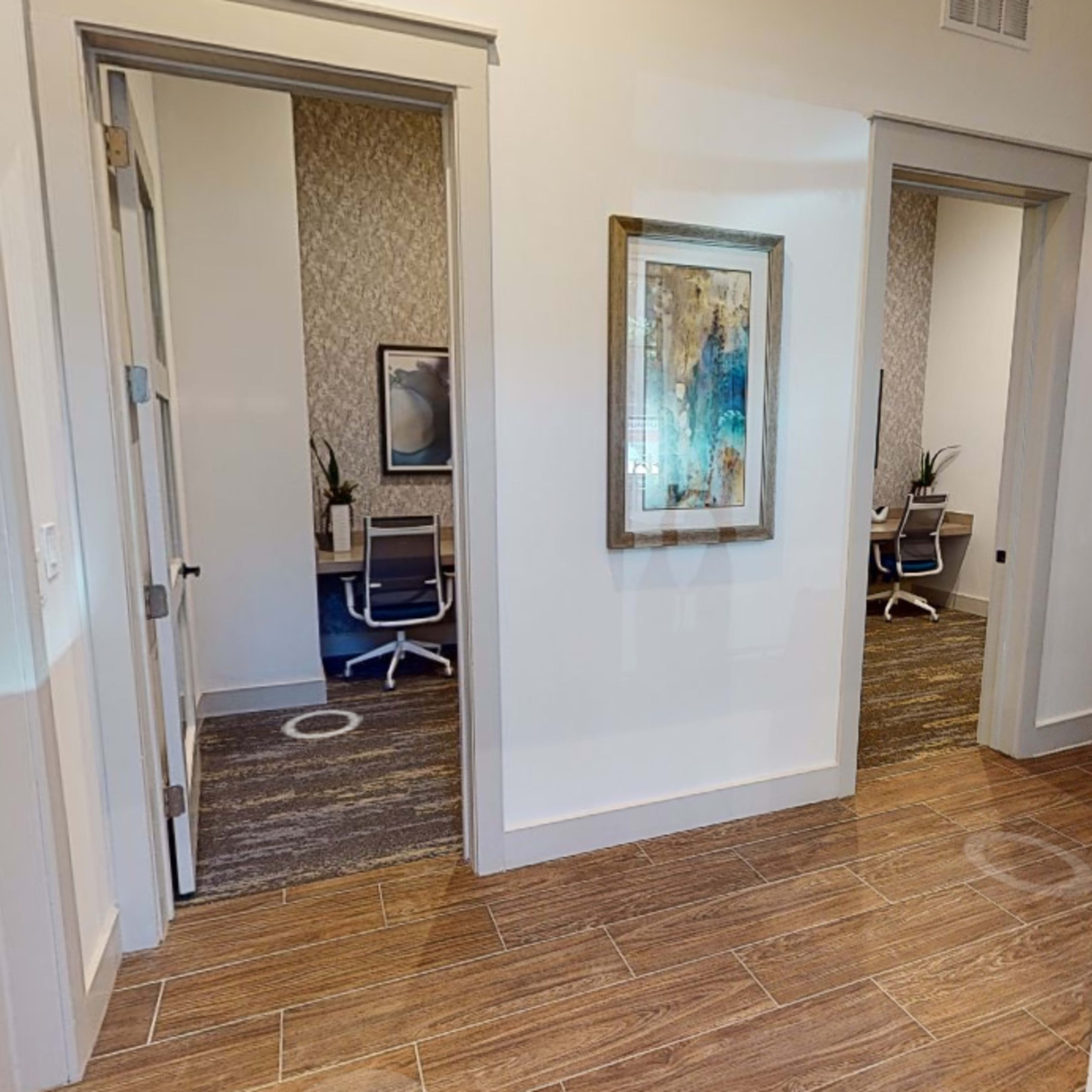 A hallway with two open doorways leading to office spaces, featuring light-colored walls and wooden flooring.
