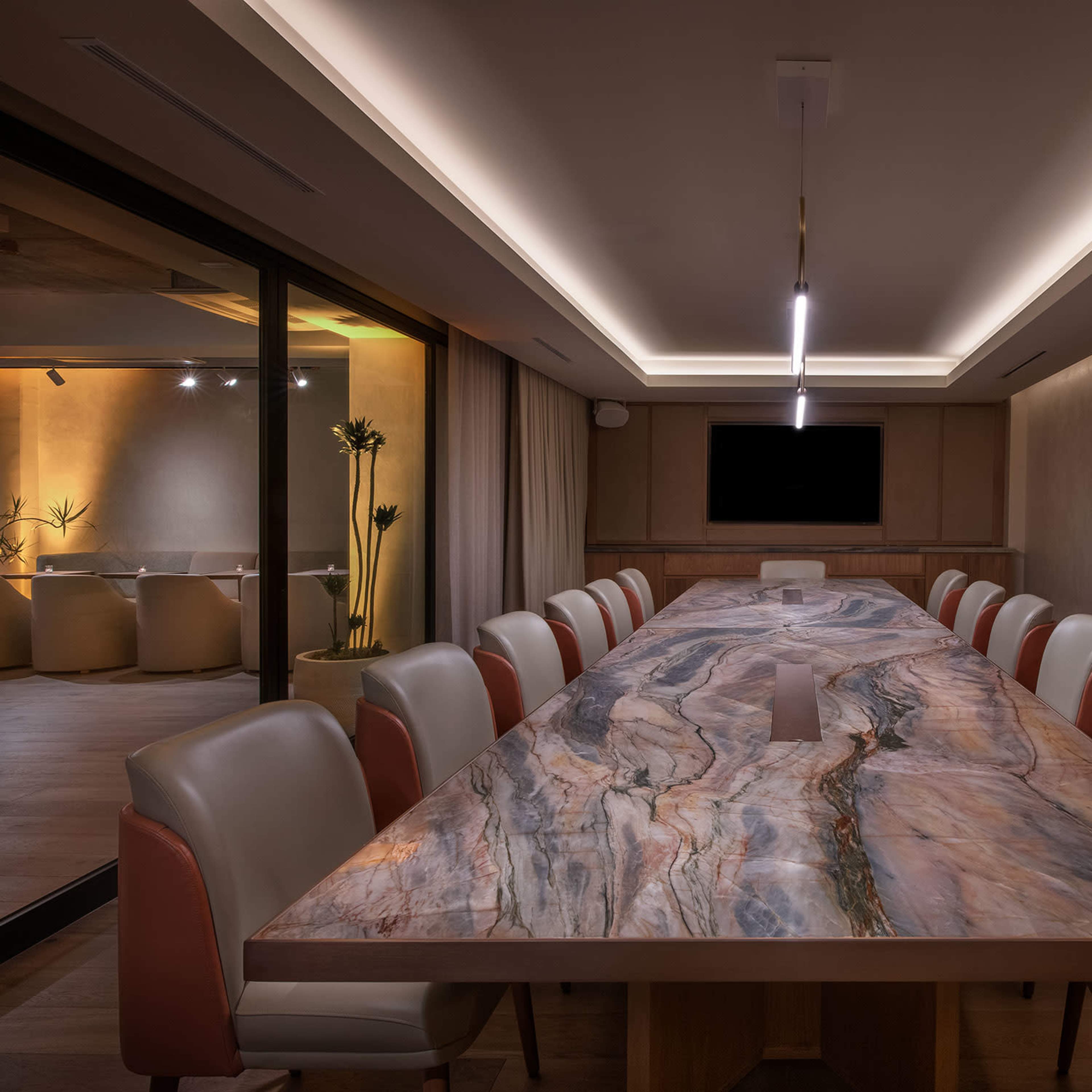 A long conference table made of patterned stone is surrounded by light-colored chairs in a spacious, well-lit meeting room.