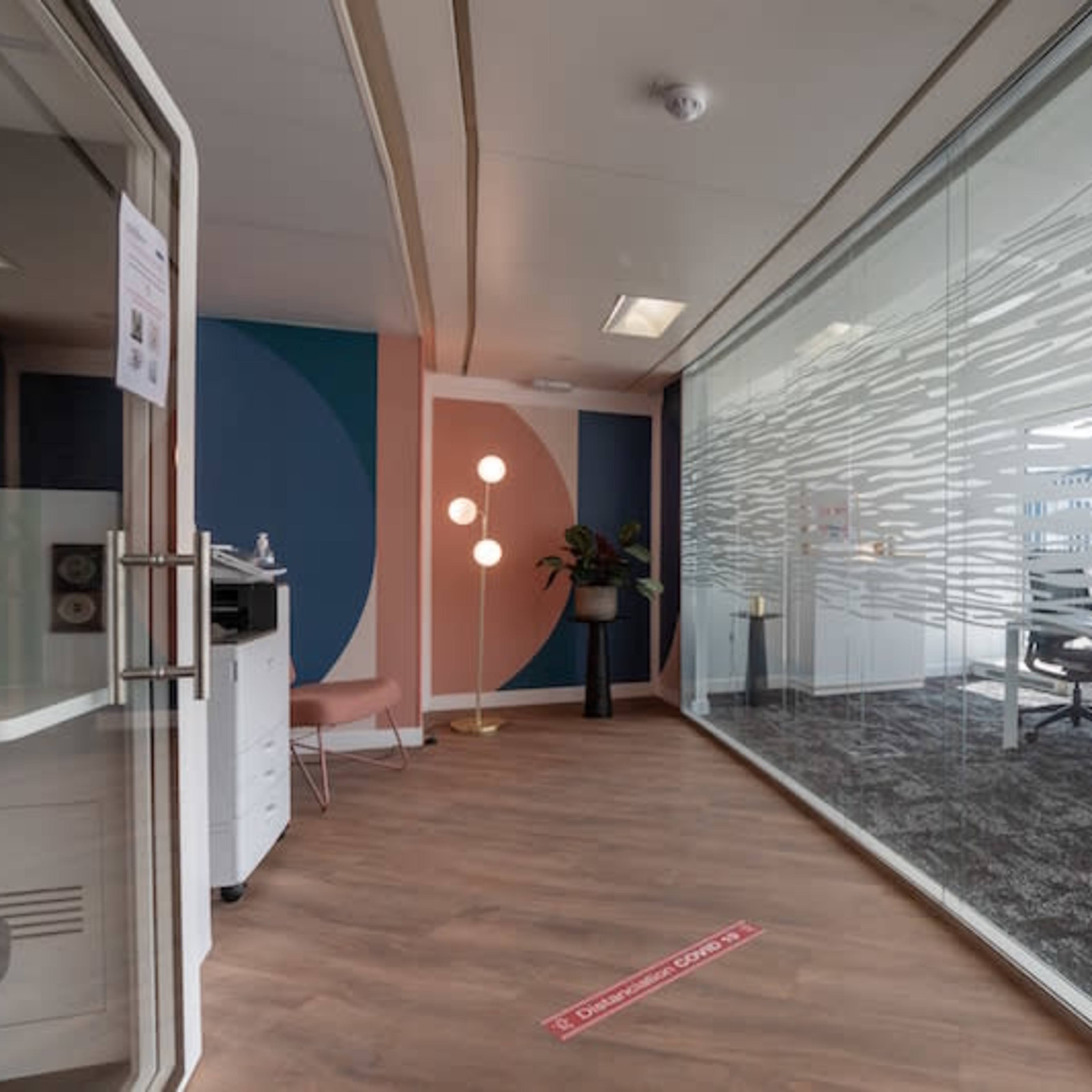A modern office space with a glass-walled conference area, wooden flooring, and a colorful accent wall.