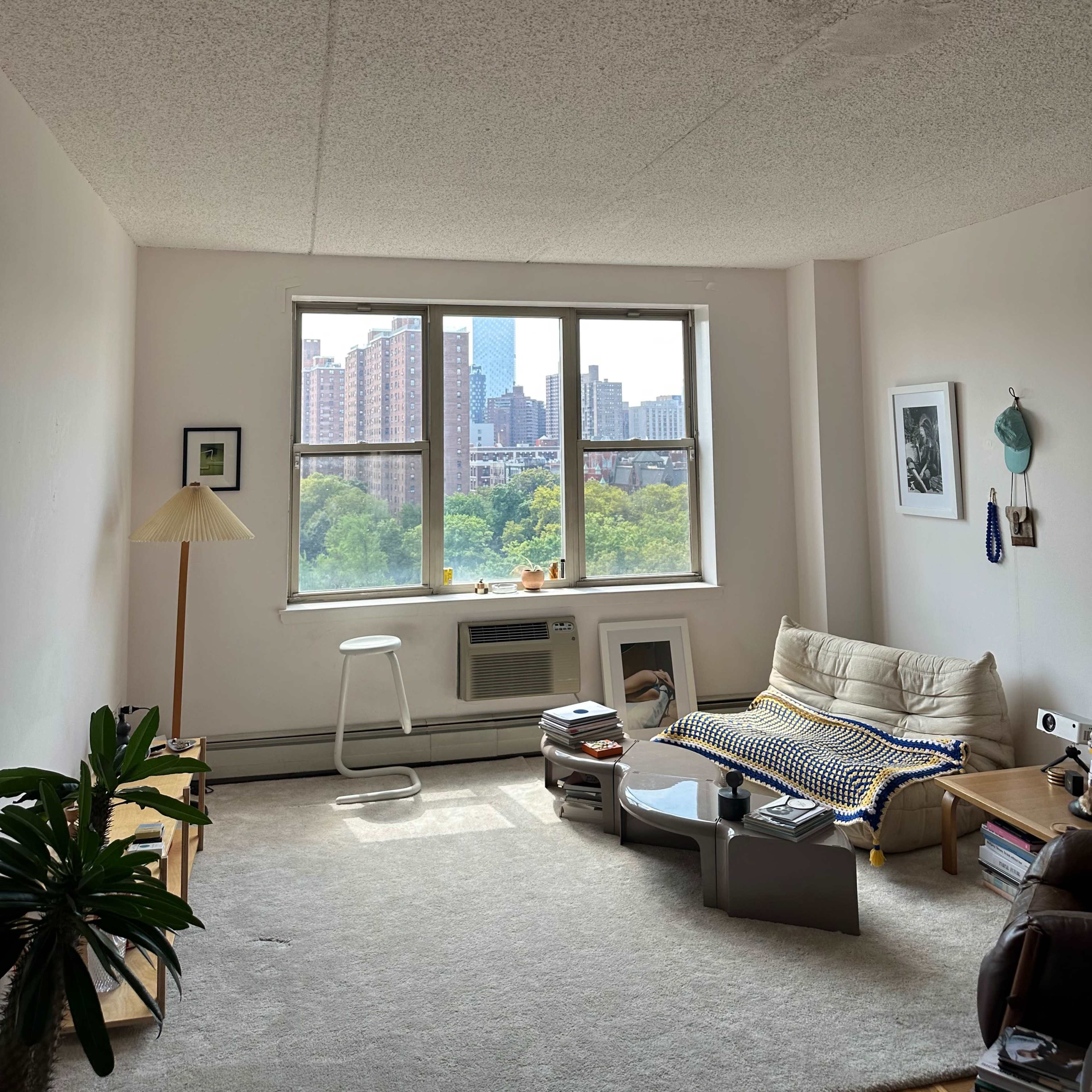 A simple living room with a sofa, coffee table, and a large window revealing a cityscape outside.