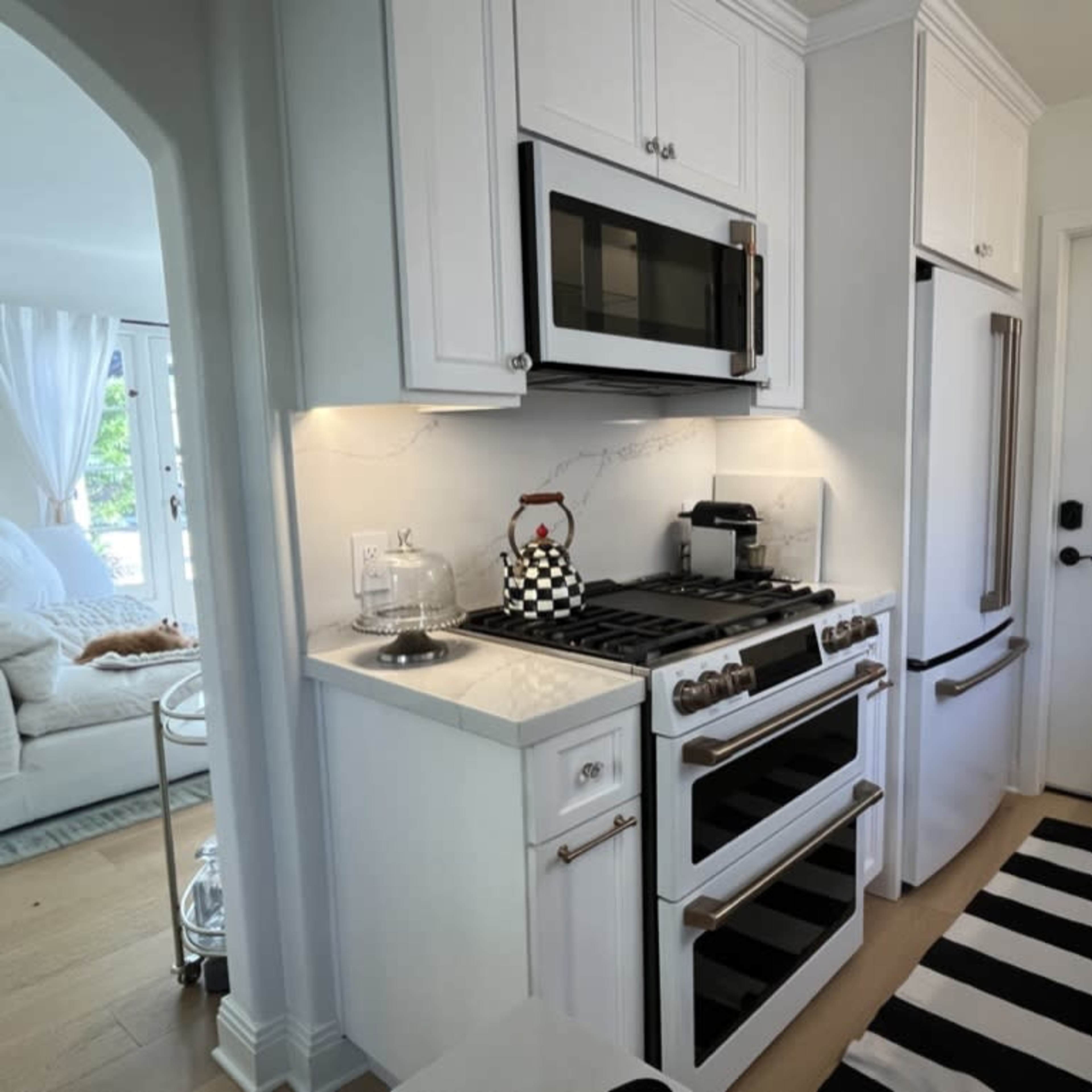 A modern kitchen features stainless steel appliances, white cabinetry, and a striped rug on the floor.