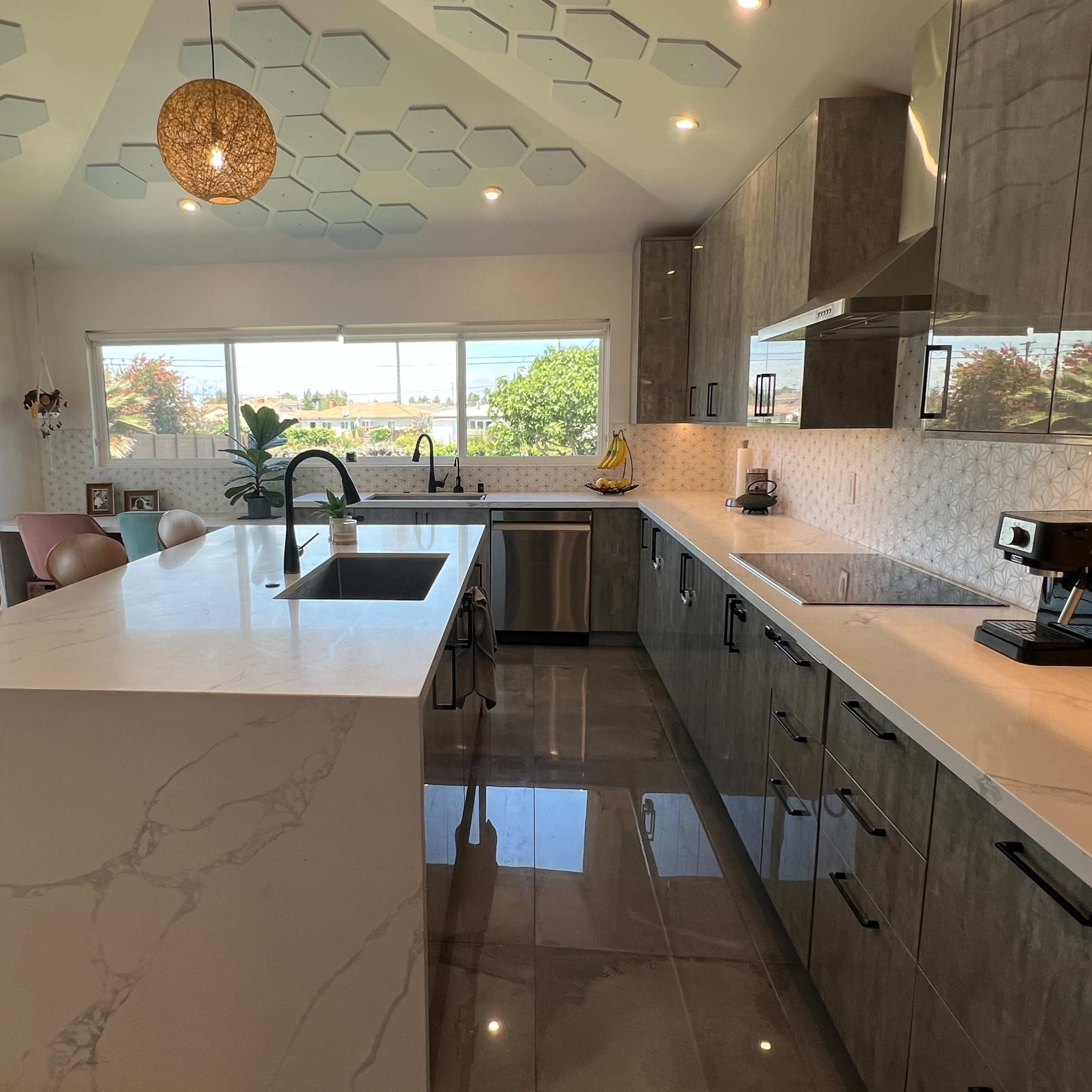 A modern kitchen with gray cabinetry, a large marble island, and a hexagonal ceiling design, illuminated by a pendant light.