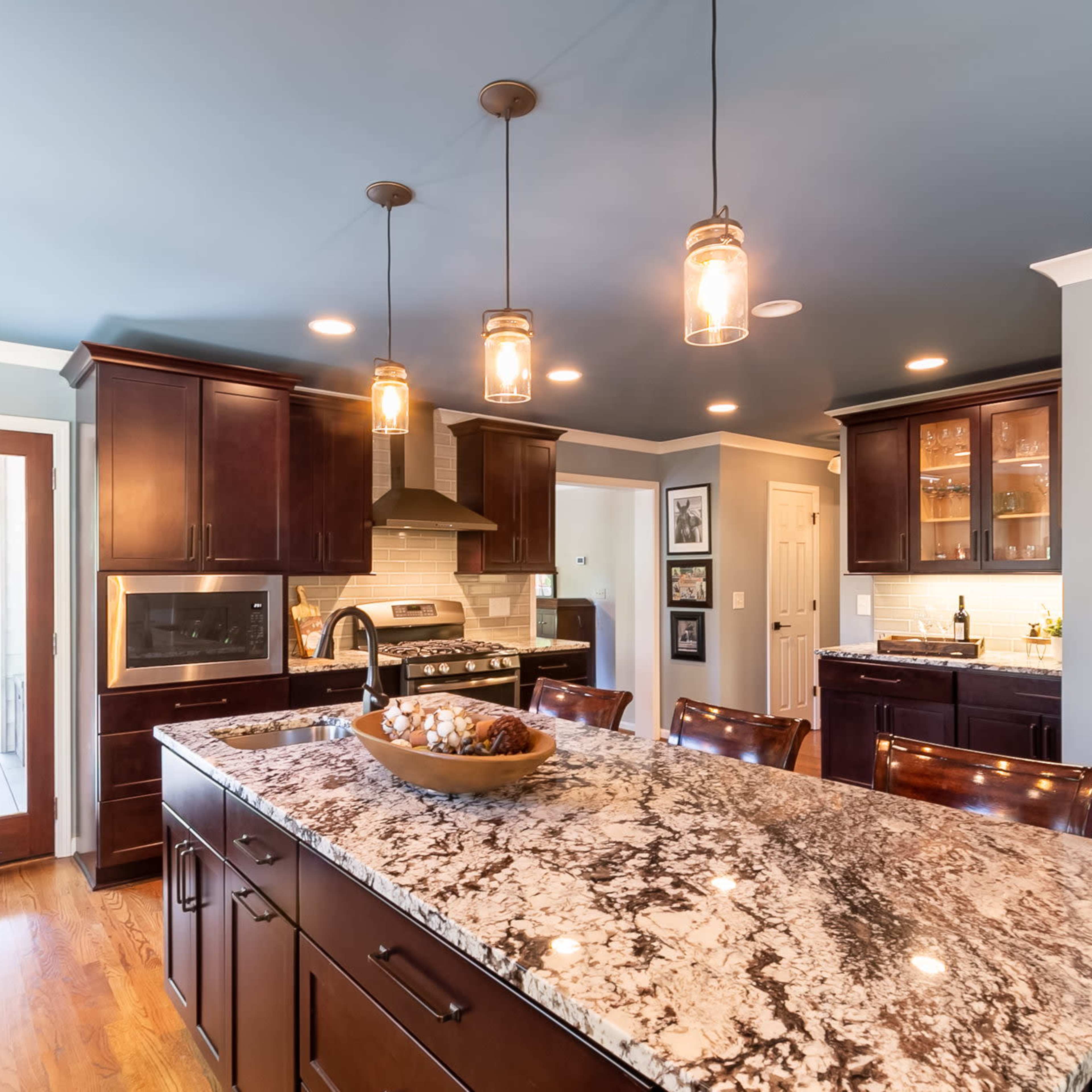 A spacious kitchen features an island with a granite countertop, dark wooden cabinets, and pendant lighting.
