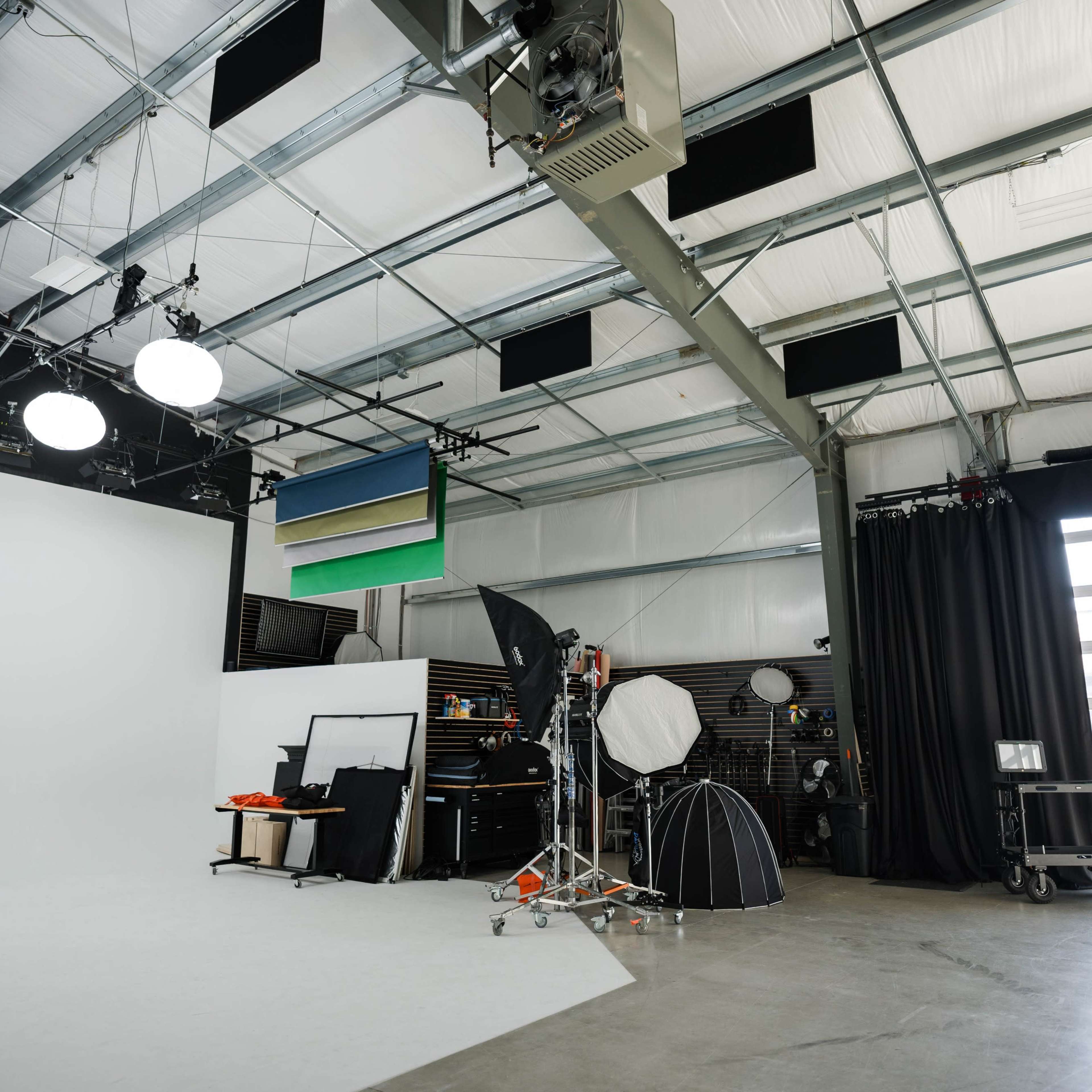 A spacious photography studio with various lighting equipment, a blank white backdrop, and a large glass door allowing natural light to enter.
