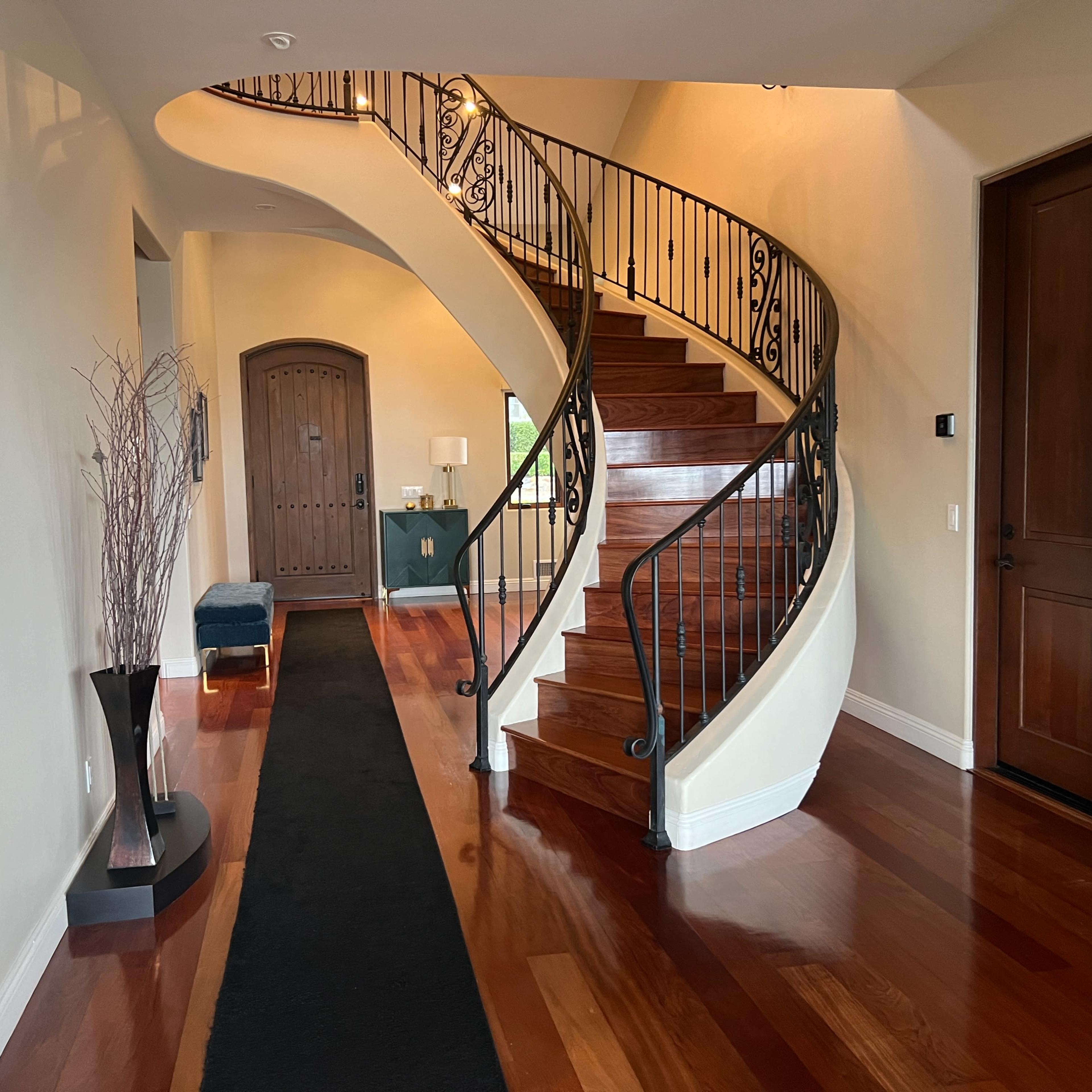 A curved wooden staircase with wrought iron railings ascends from a spacious entryway featuring a dark runner rug and decorative accents.