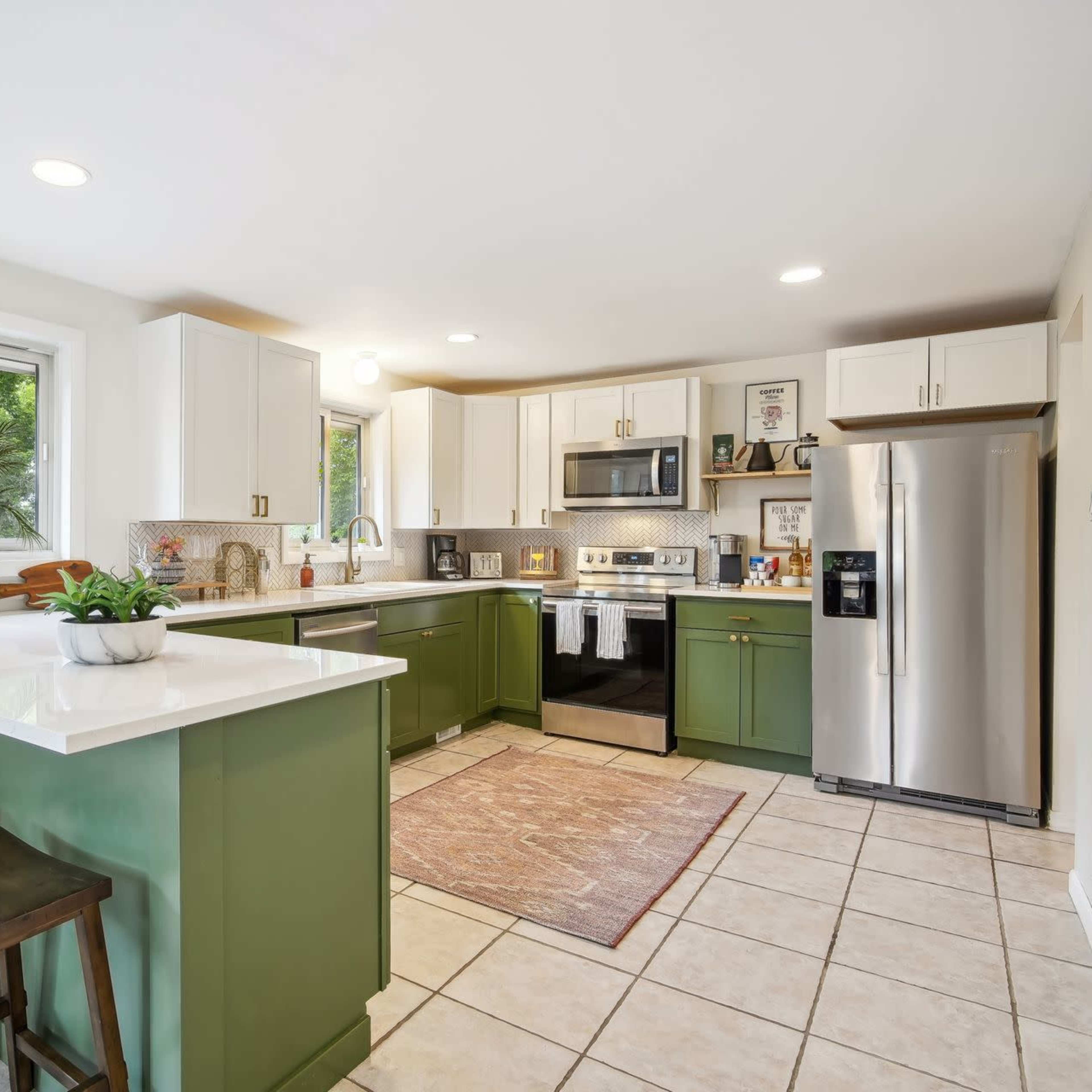 A bright kitchen features green cabinets, stainless steel appliances, and a large window overlooking greenery.
