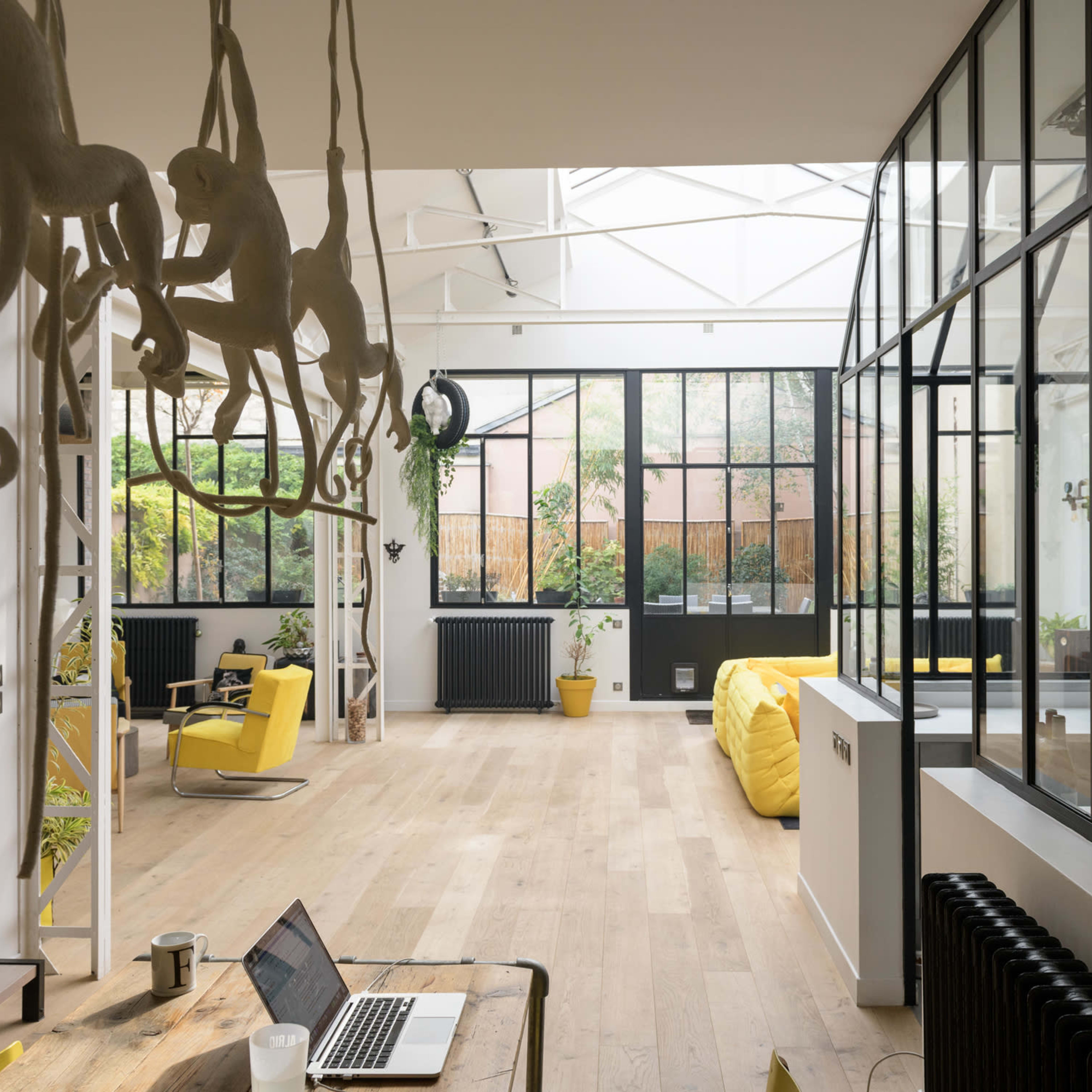A spacious, modern open-plan interior featuring large windows, a wooden floor, and hanging monkey sculptures.