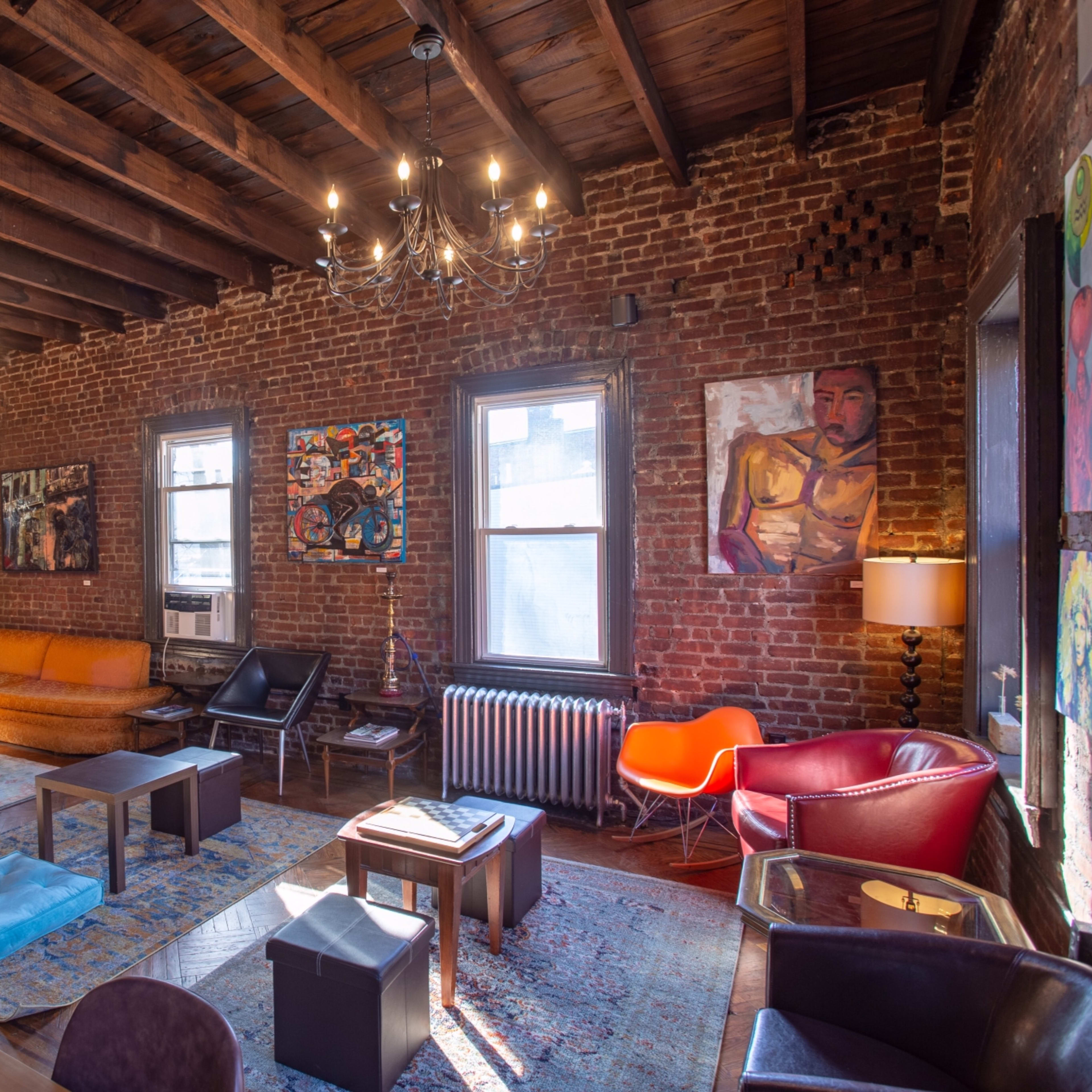 A spacious living room with exposed brick walls, wooden beams, and various seating arrangements, including a blue couch, an orange sofa, and a red chair.
