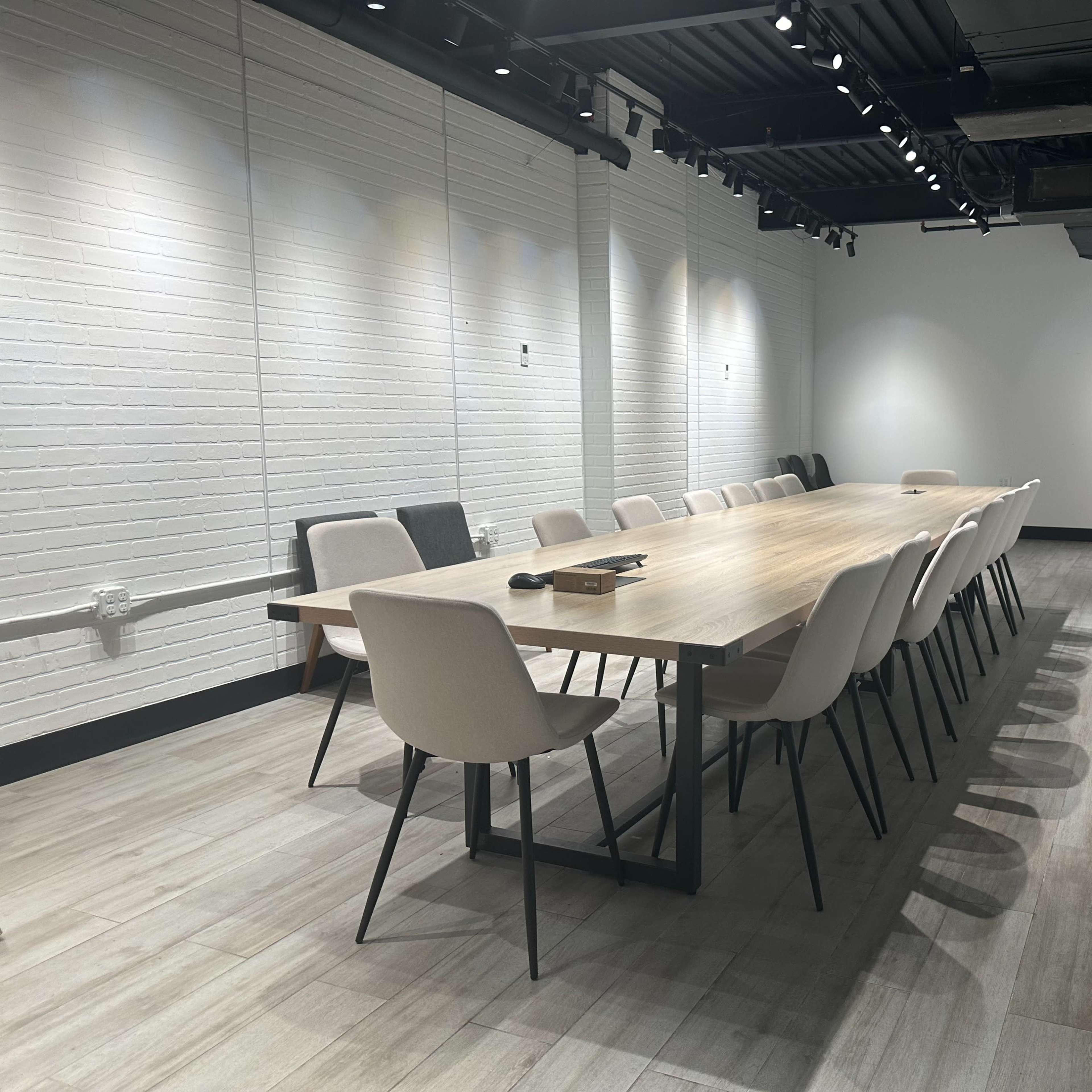 A long wooden conference table is set with chairs along each side in a brightly lit meeting room with white brick walls.