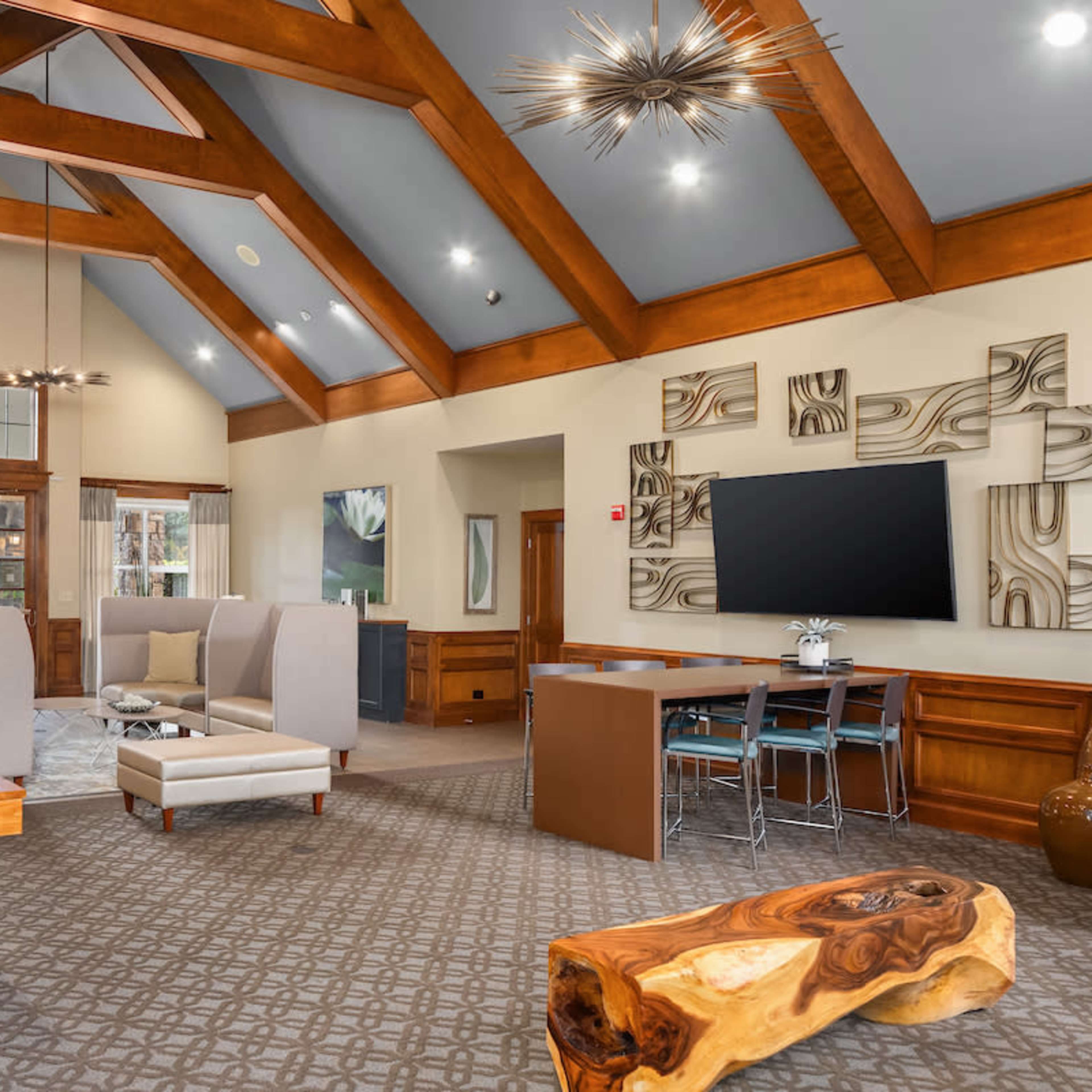 A spacious lobby area with wooden beams, modern seating arrangements, and a pool table, surrounded by large windows and contemporary decor.