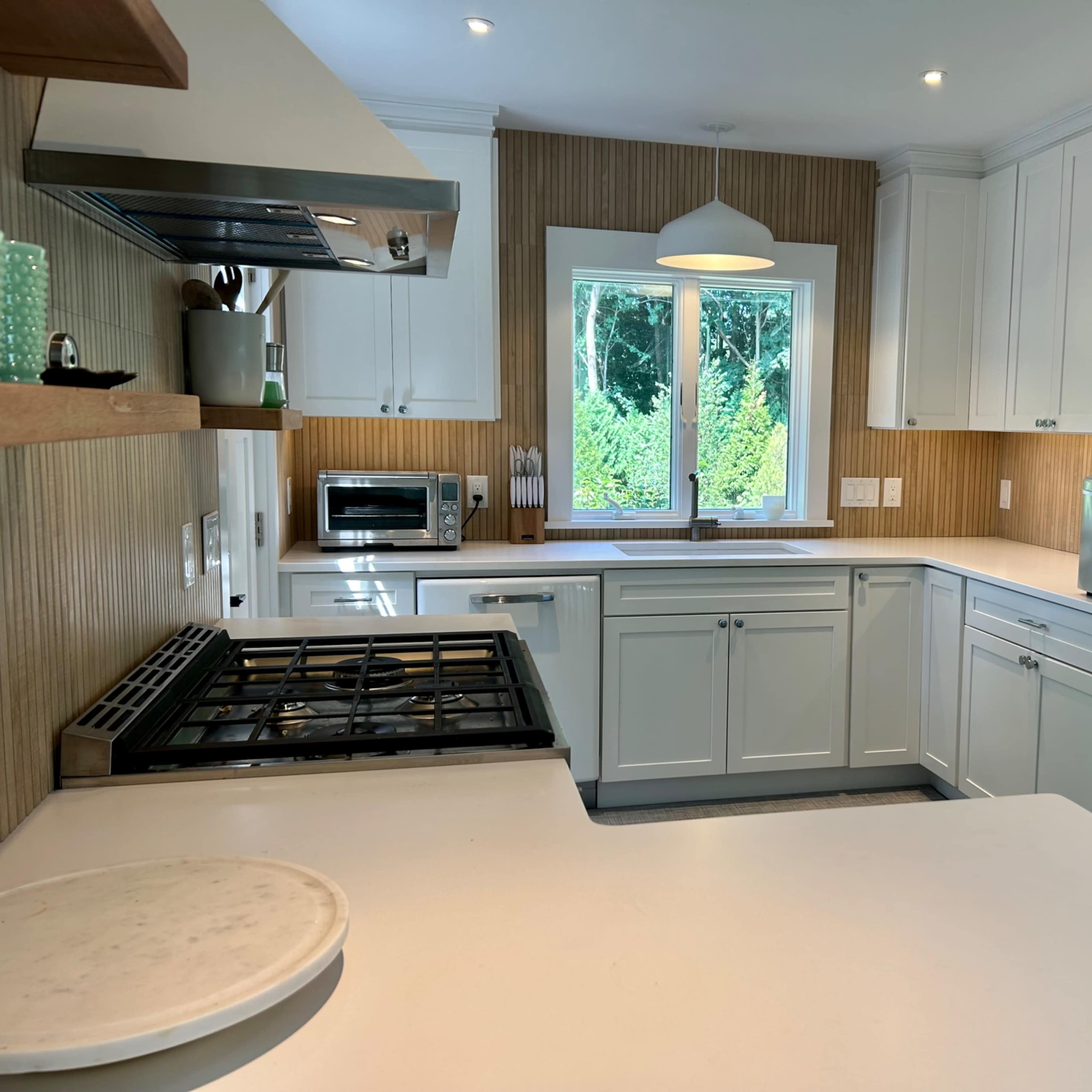 A modern kitchen features white cabinetry, wooden accents, and a retro-style blue refrigerator, with a window overlooking greenery.