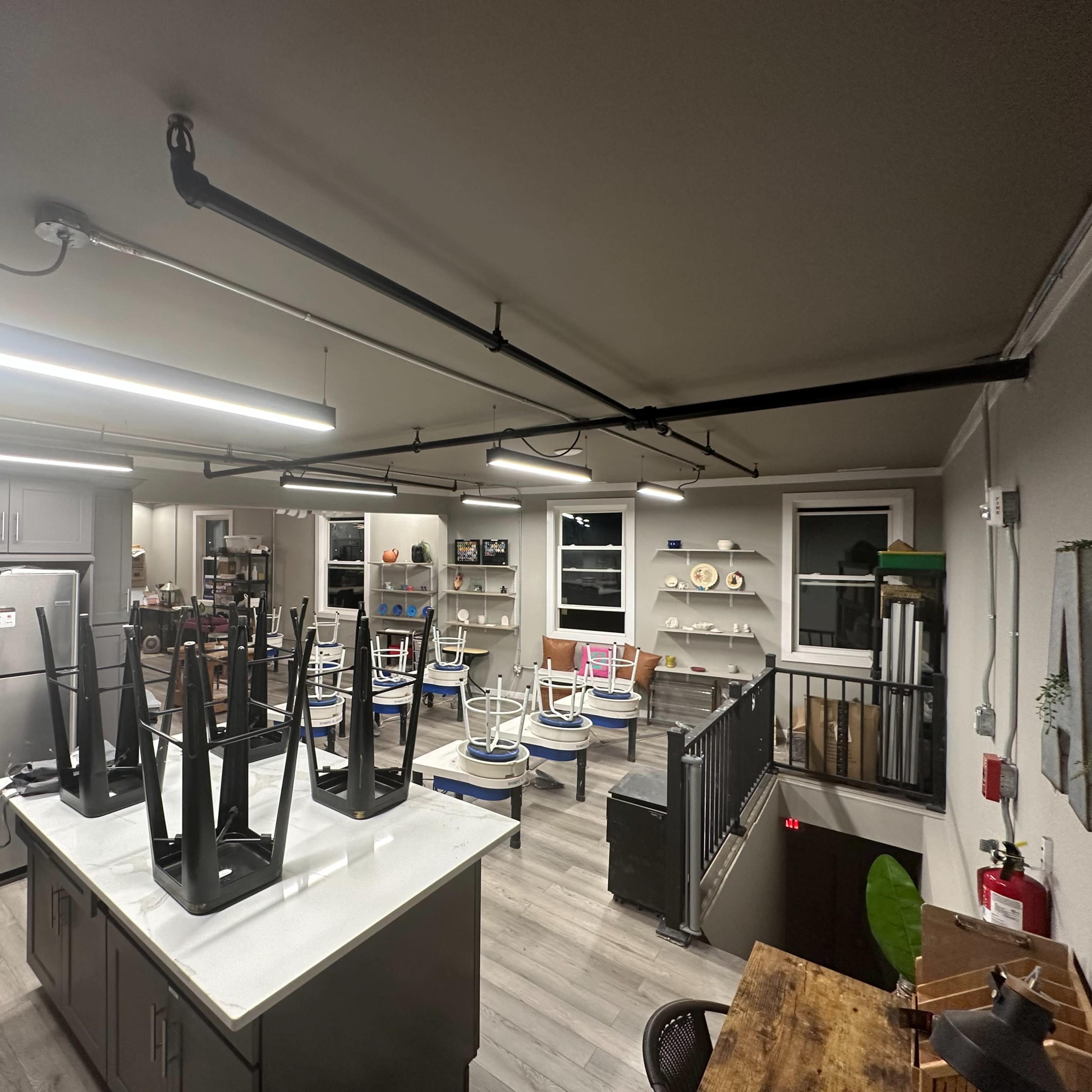 A spacious room with kitchen and dining areas, featuring overturned chairs on tables and a gray color scheme.