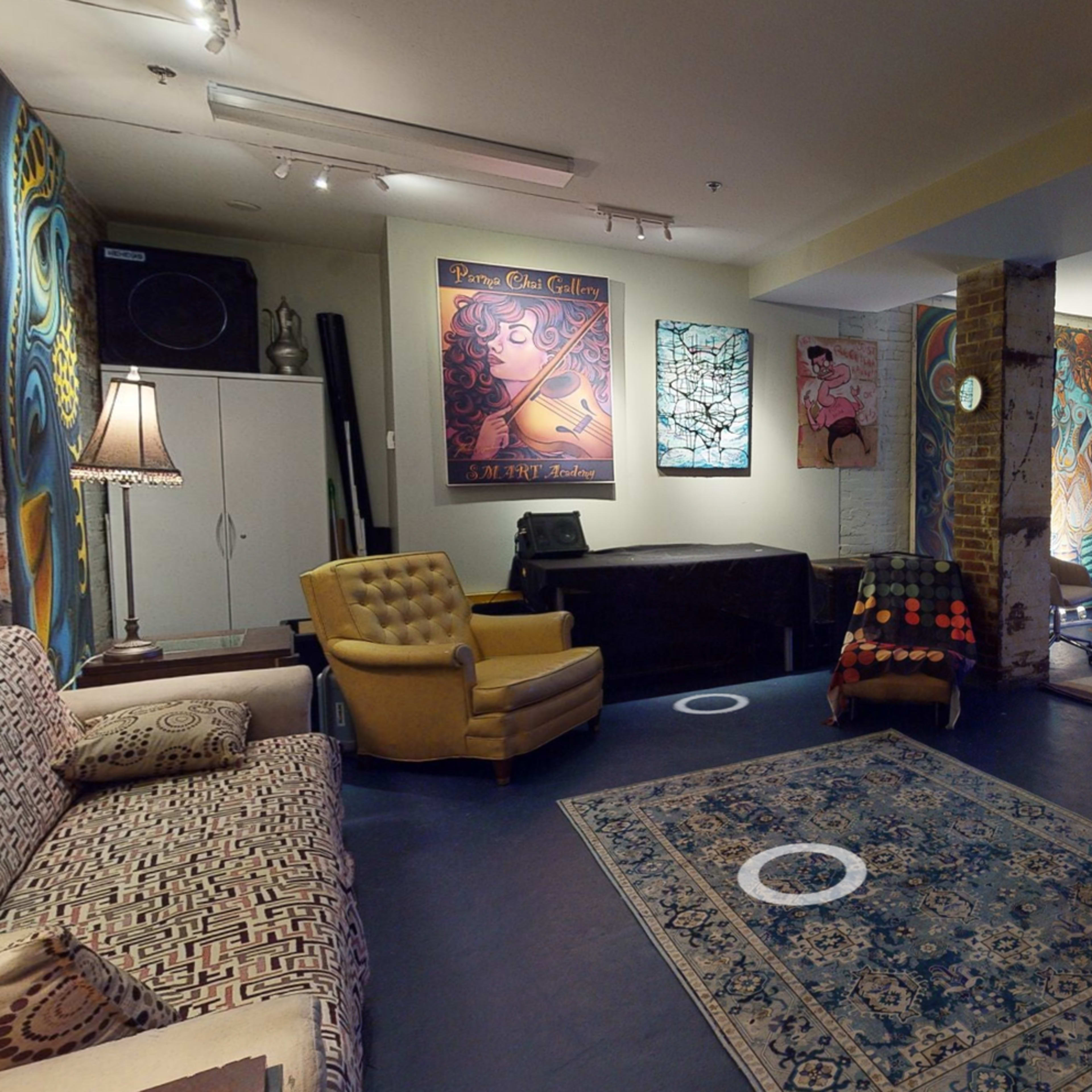 A spacious art studio or gallery with various artworks displayed on the walls, patterned rugs on the floor, and a mix of seating arrangements.