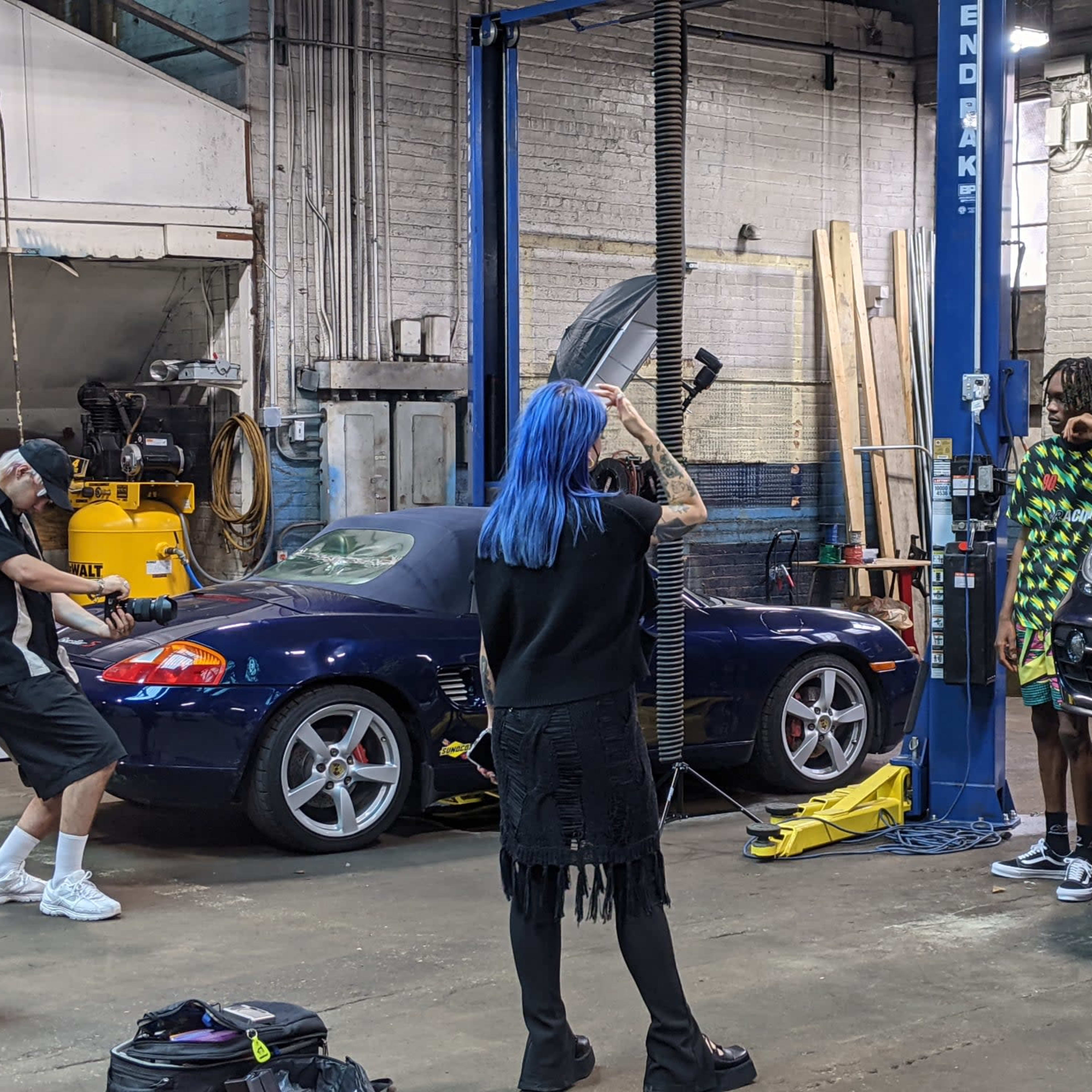 A photographer captures a model posing next to two sports cars in an auto shop.