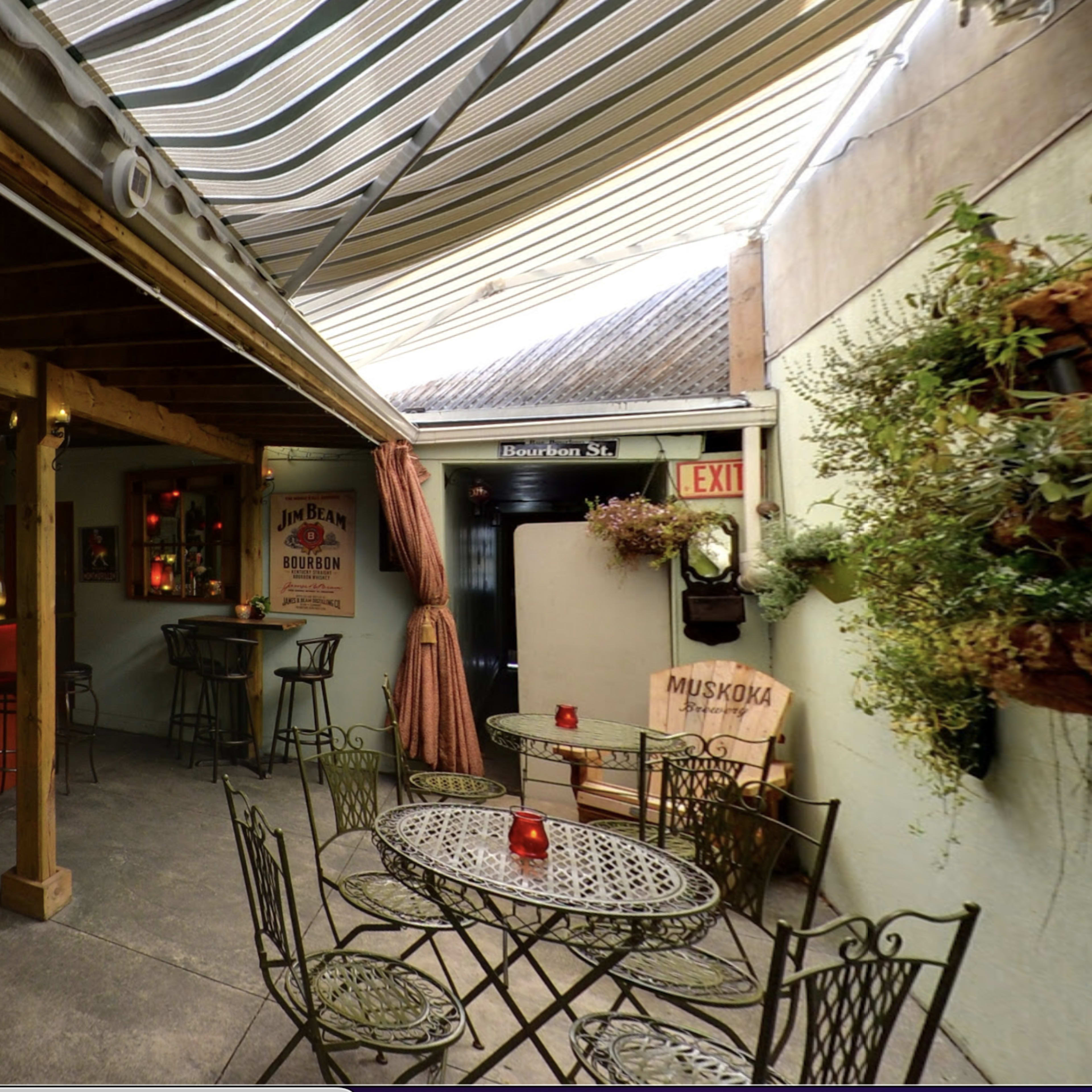 A cozy, dimly lit indoor bar area with a counter, high stools, and small tables surrounded by walls decorated with vintage signs.