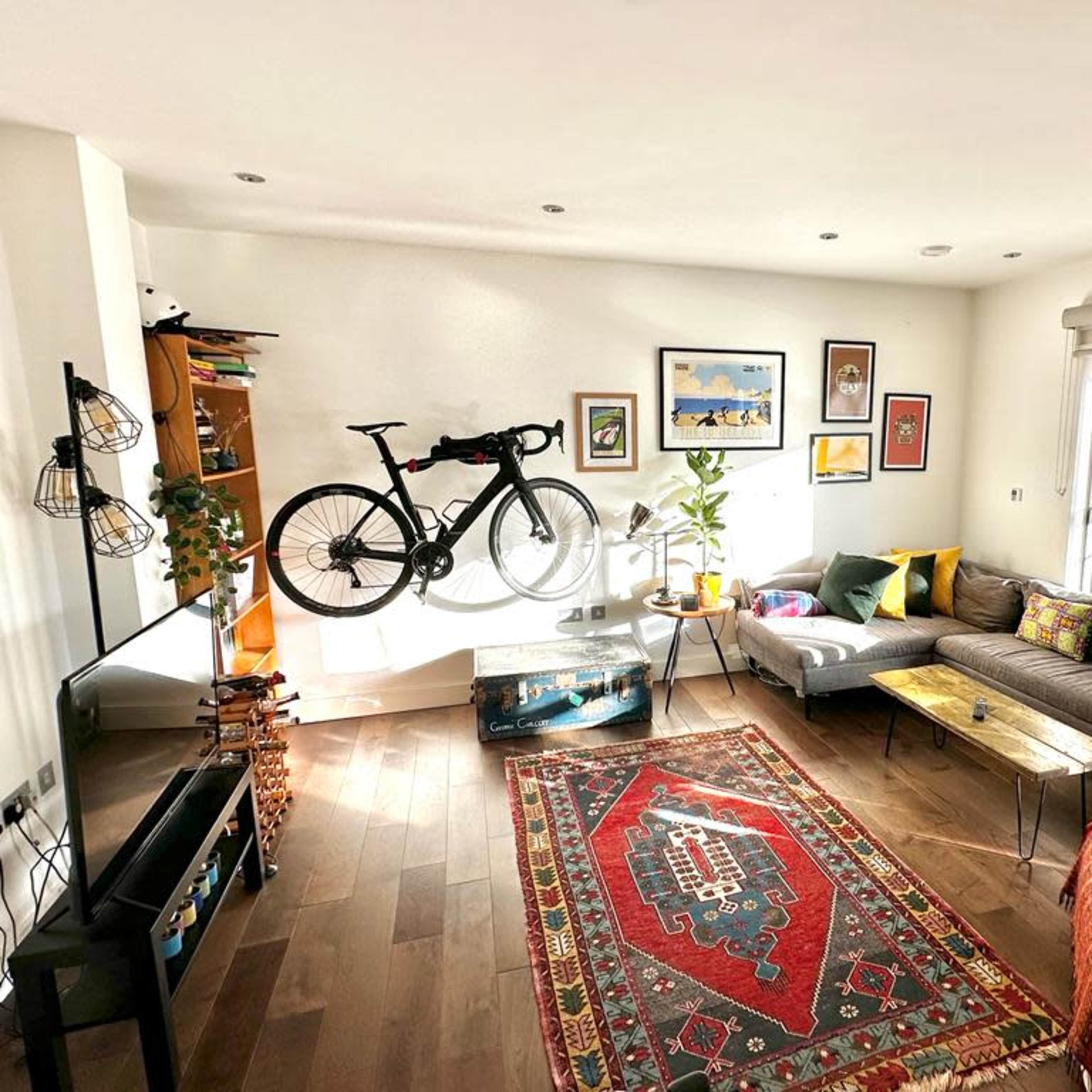 A modern living room featuring a gray sectional sofa, a bicycle mounted on the wall, a rug on the wooden floor, and large windows allowing natural light to fill the space.