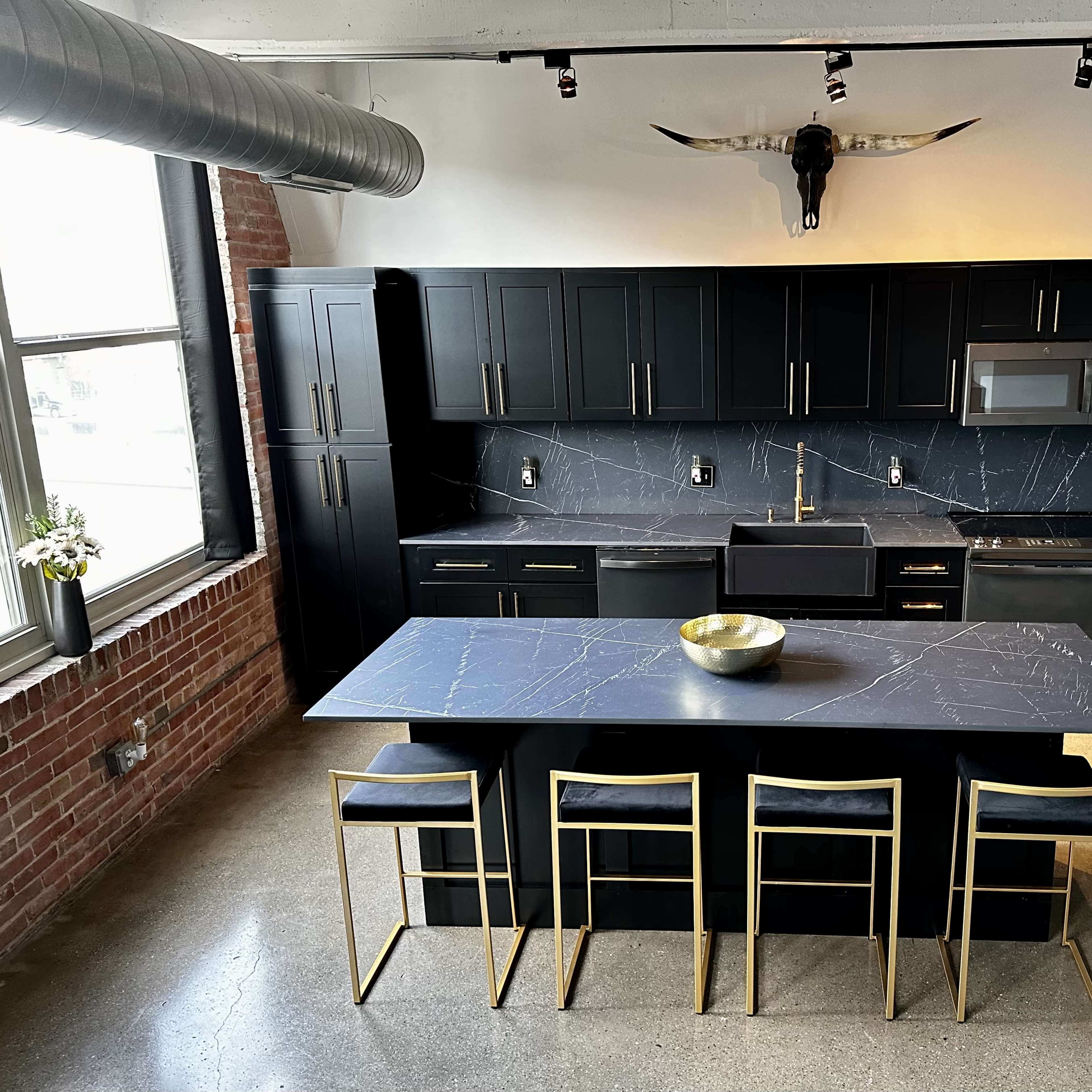 A modern kitchen with black cabinetry, a marble countertop, and gold-accented bar stools arranged around a large island.