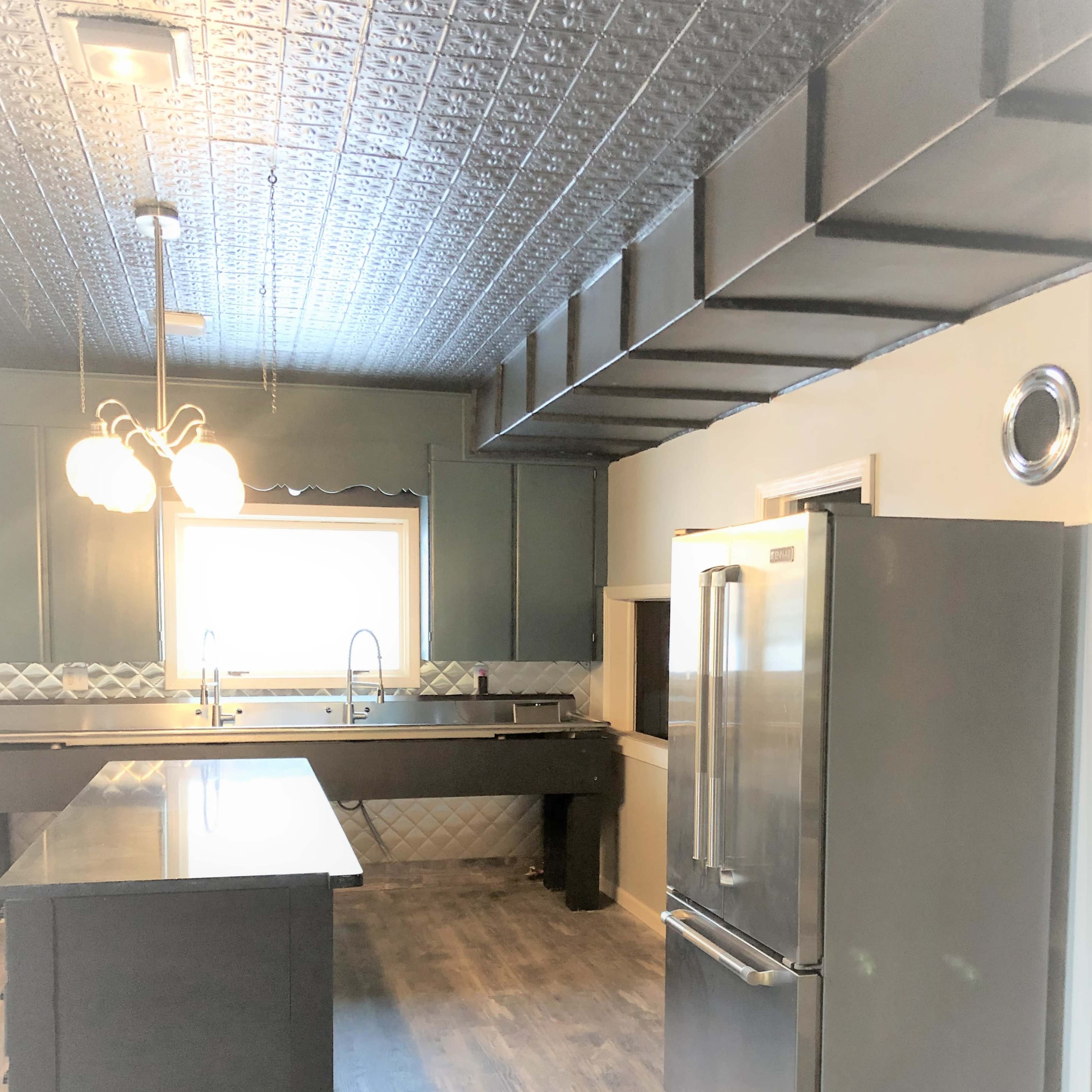 A modern kitchen with a large window, a stainless steel refrigerator, a dark countertop, and pendant lighting.