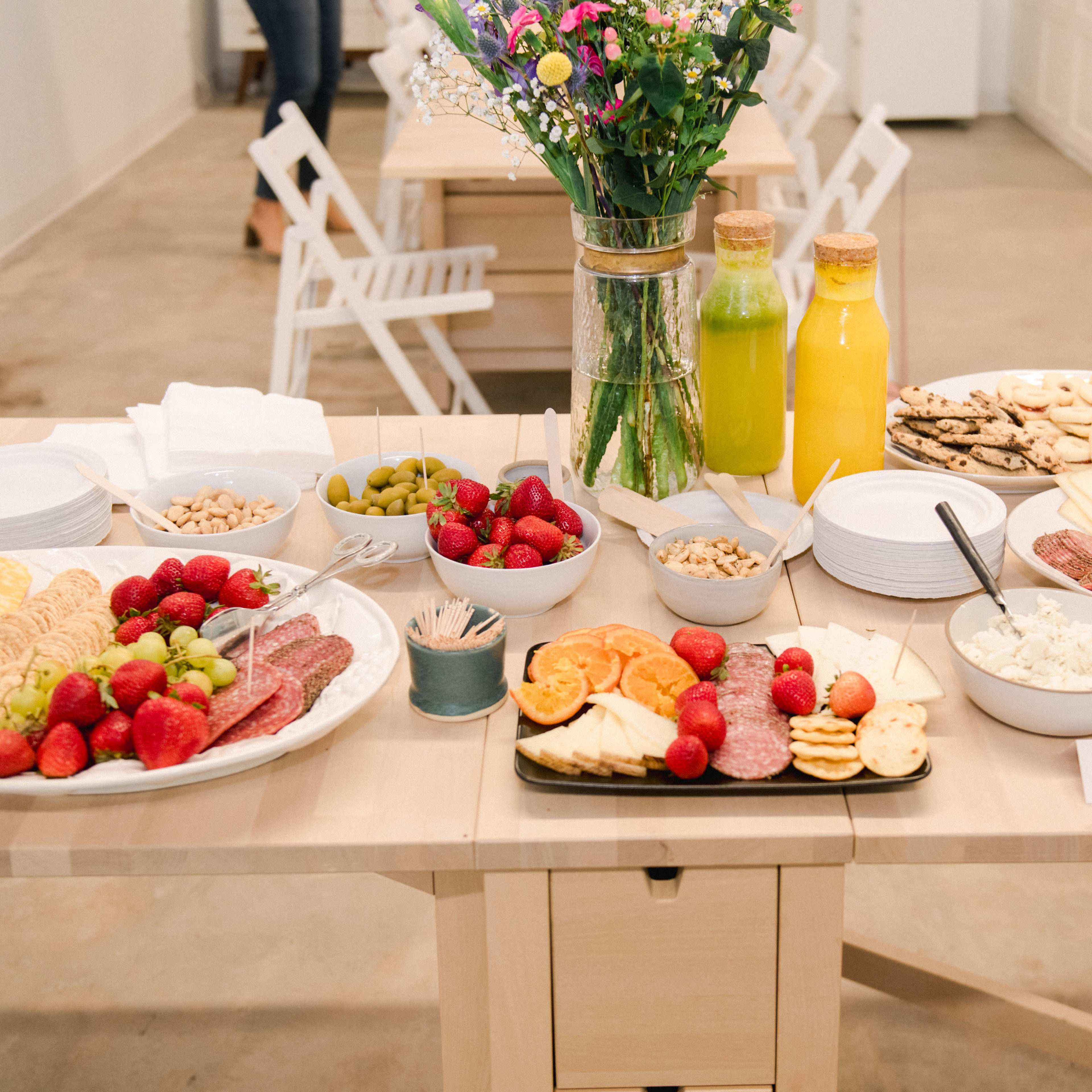 A table is set with a variety of food items, including cheeses, meats, fruits, nuts, and drinks, arranged neatly for a gathering.