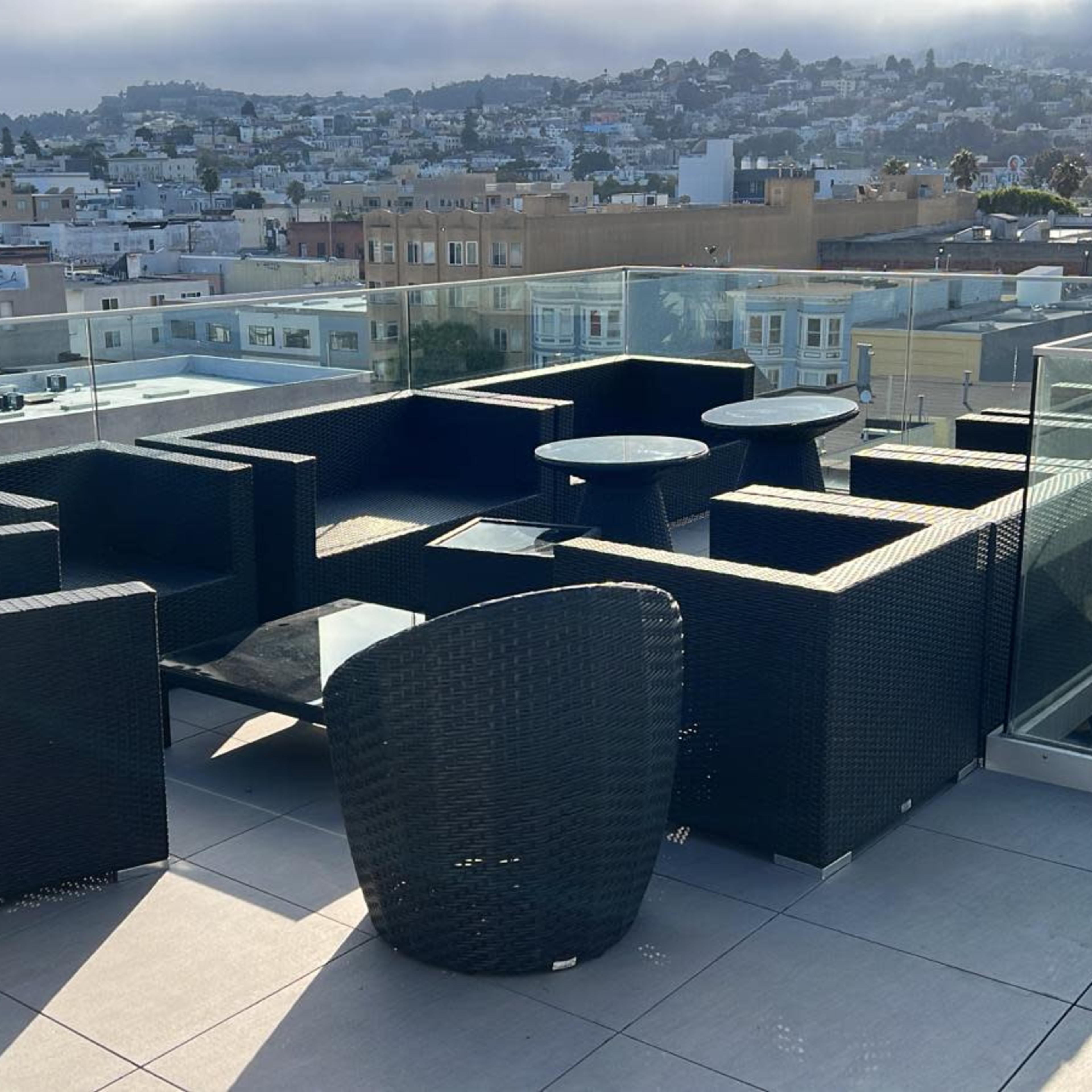A rooftop terrace features a modern seating area with black wicker furniture and a view of the city in the background.