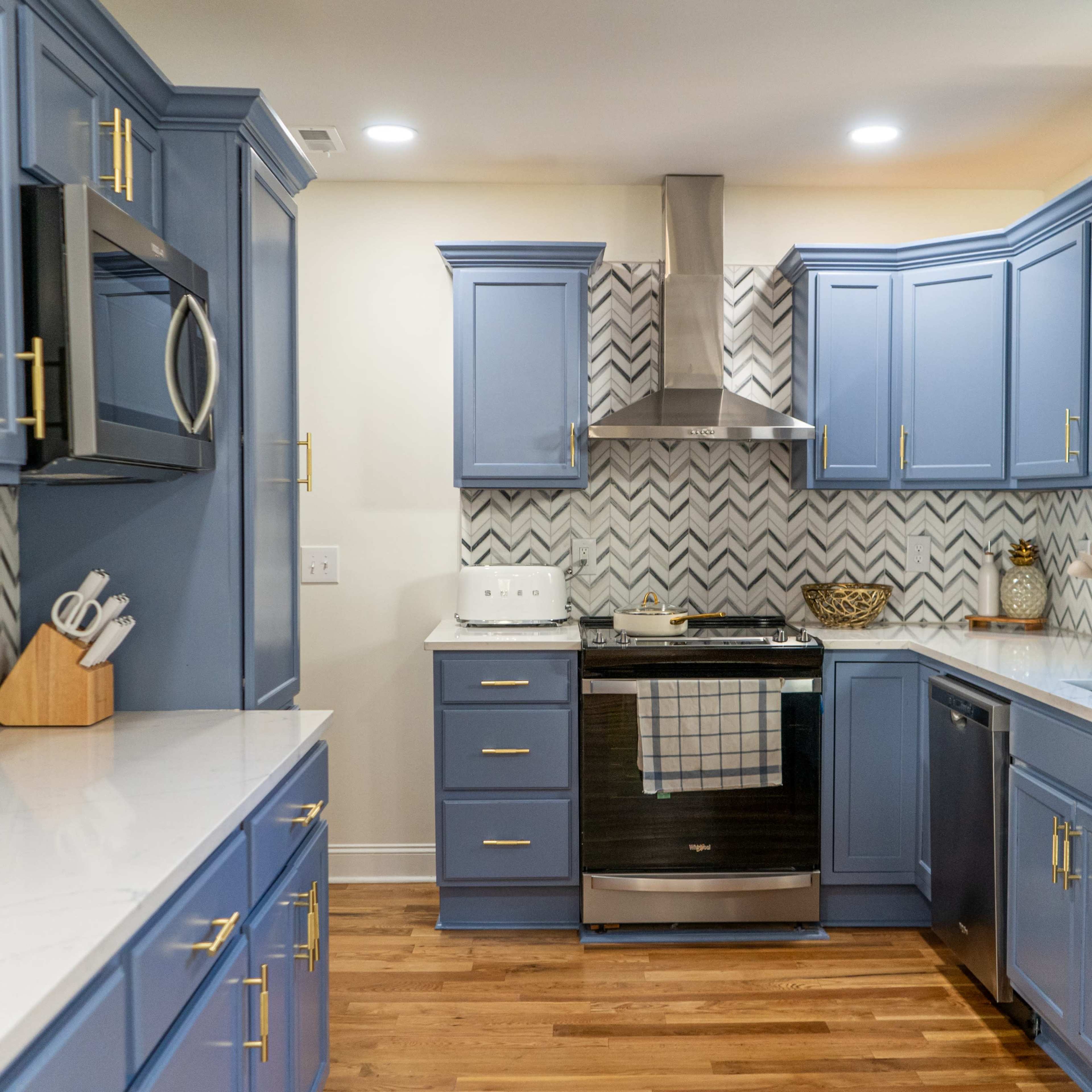 A modern kitchen features blue cabinetry, a stainless steel refrigerator, and a chevron-patterned backsplash.