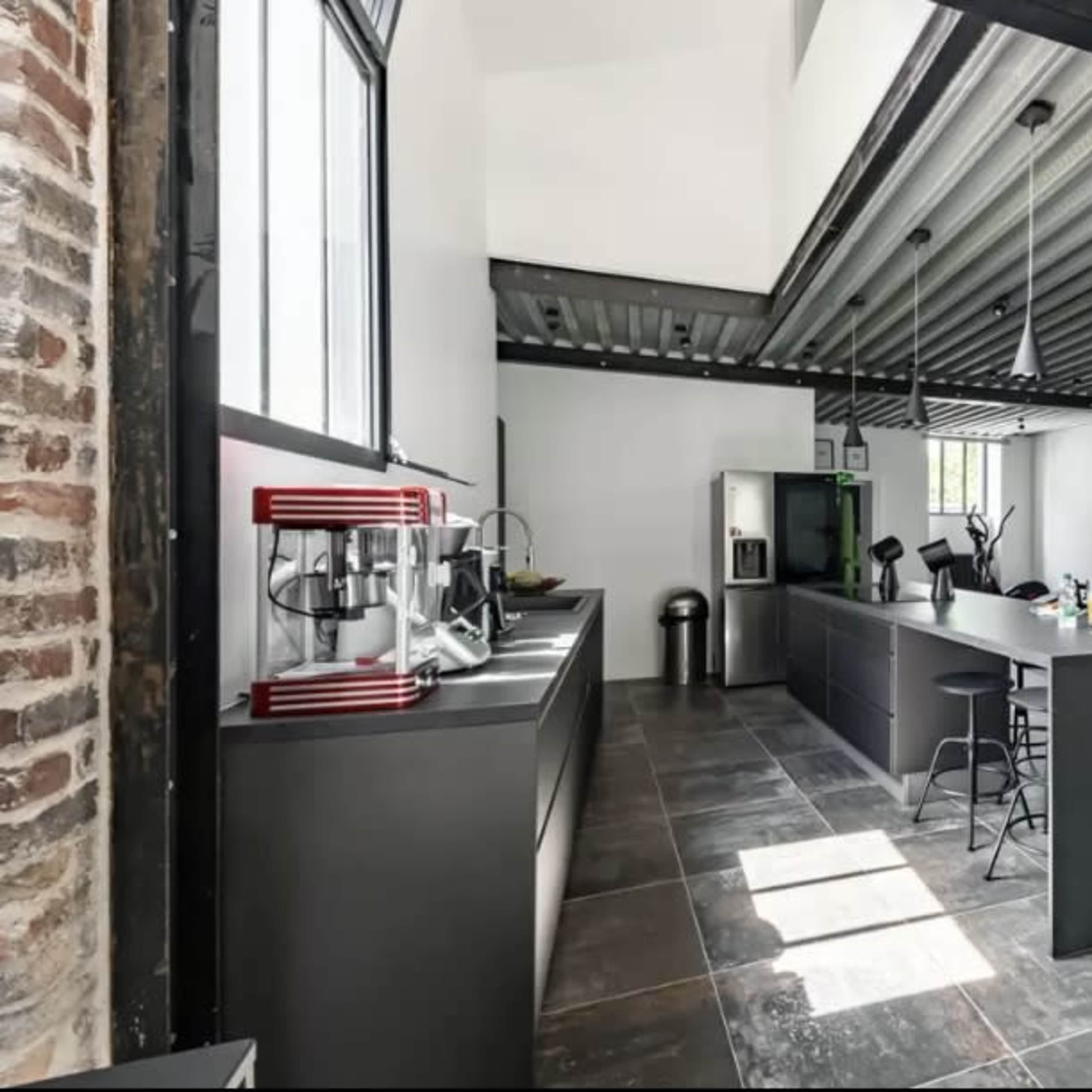 A modern kitchen area with black cabinetry, stainless steel appliances, and a staircase that leads to an upper level.