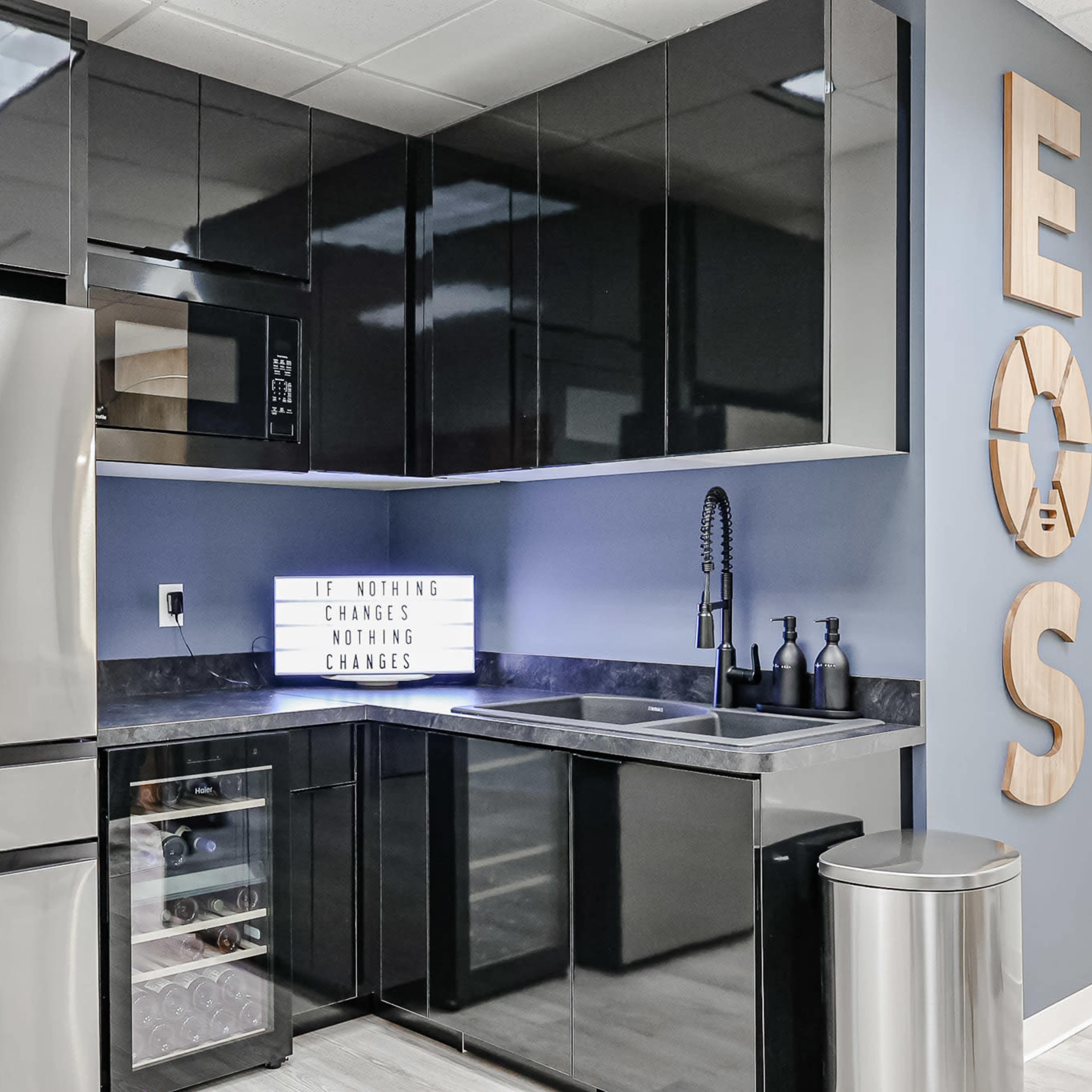 A modern kitchen with sleek black cabinetry, stainless steel appliances, and a decorative sign displaying the phrase "IF NOTHING CHANGES NOTHING CHANGES."
