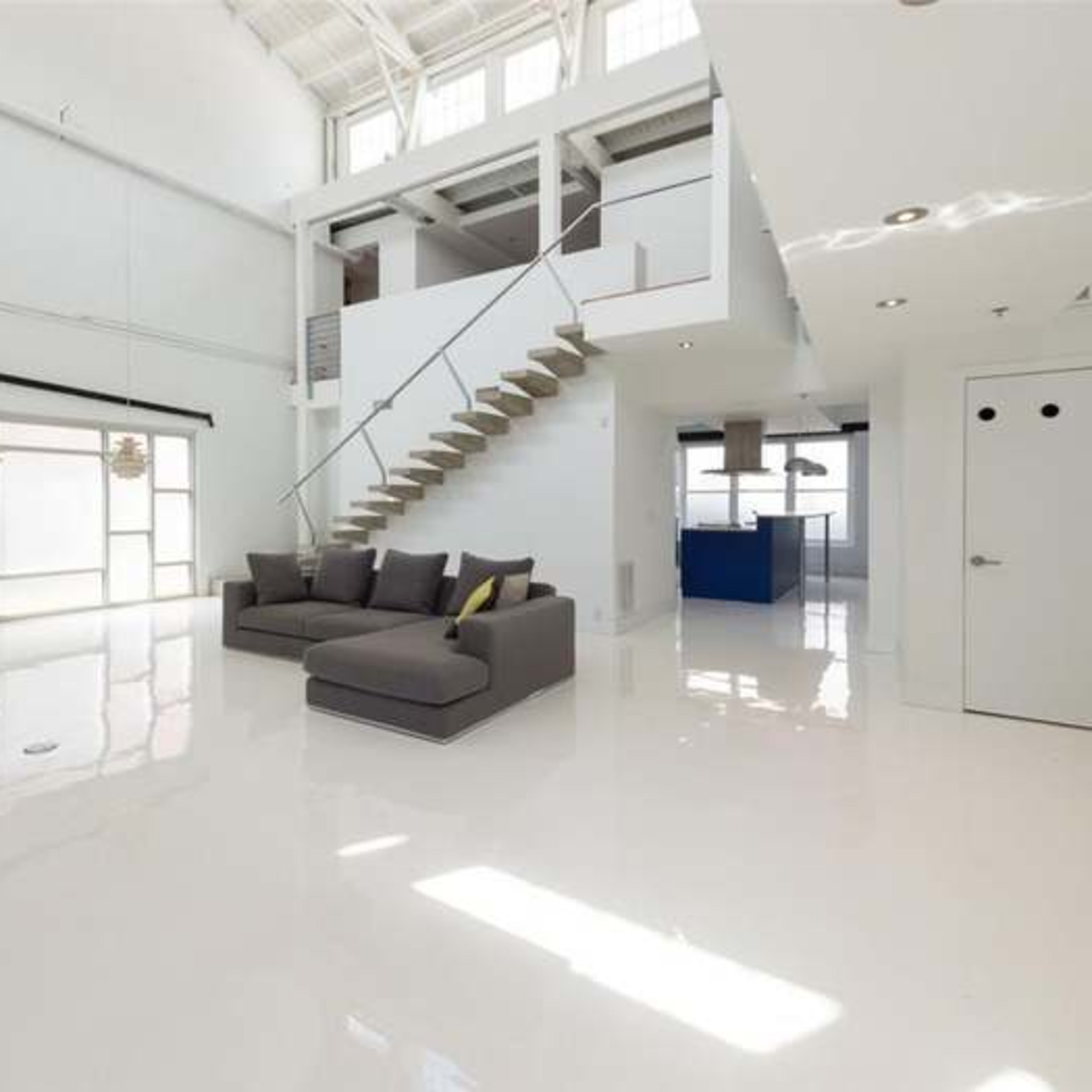 A modern, spacious living area with a bright, white floor, a gray sectional sofa, and a staircase leading to an upper level.