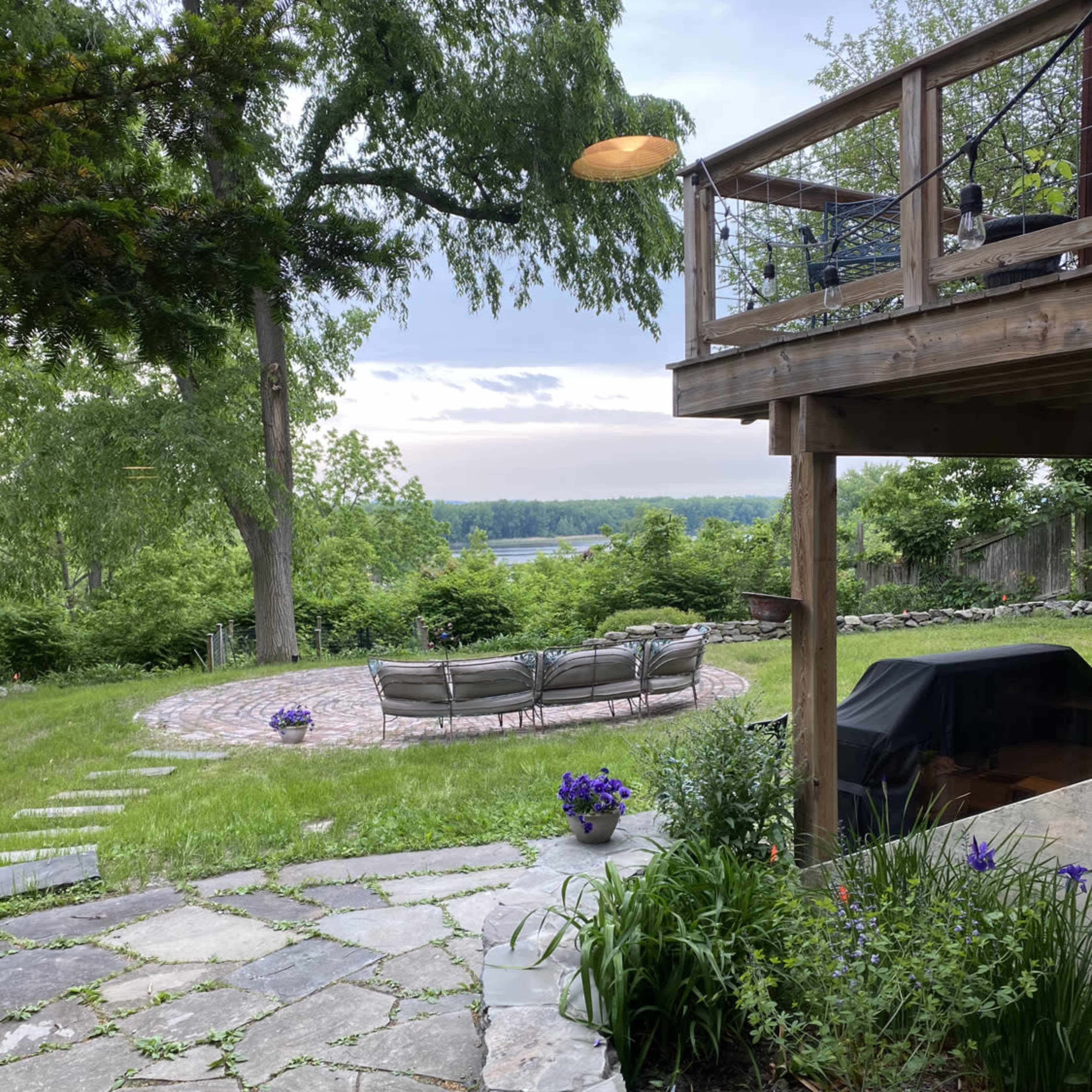 A landscaped backyard with a stone path, a seating area surrounded by greenery, and a view of a river beyond.