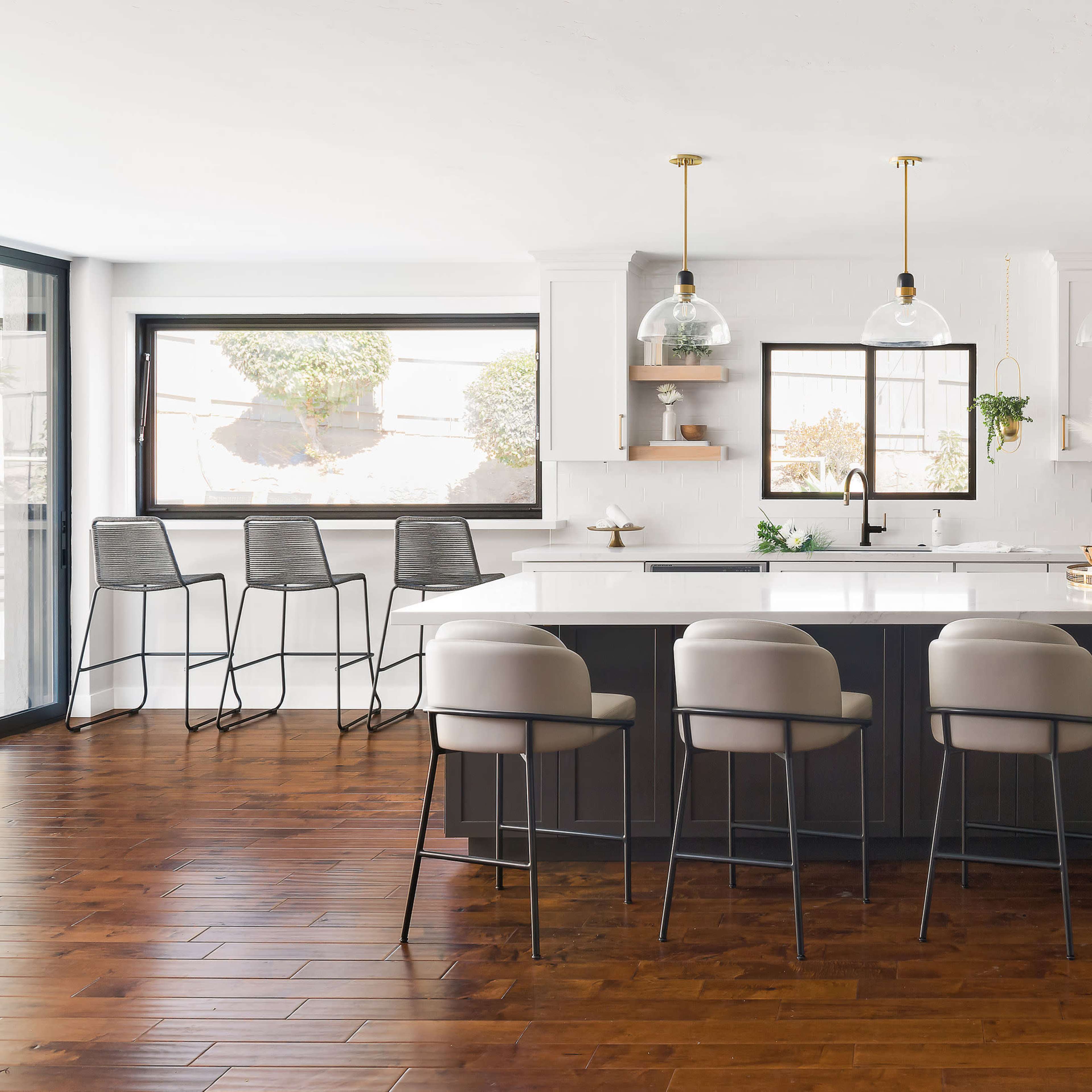 A modern kitchen features a central island with seated bar stools, pendant lighting, and a combination of white cabinetry and dark countertops.