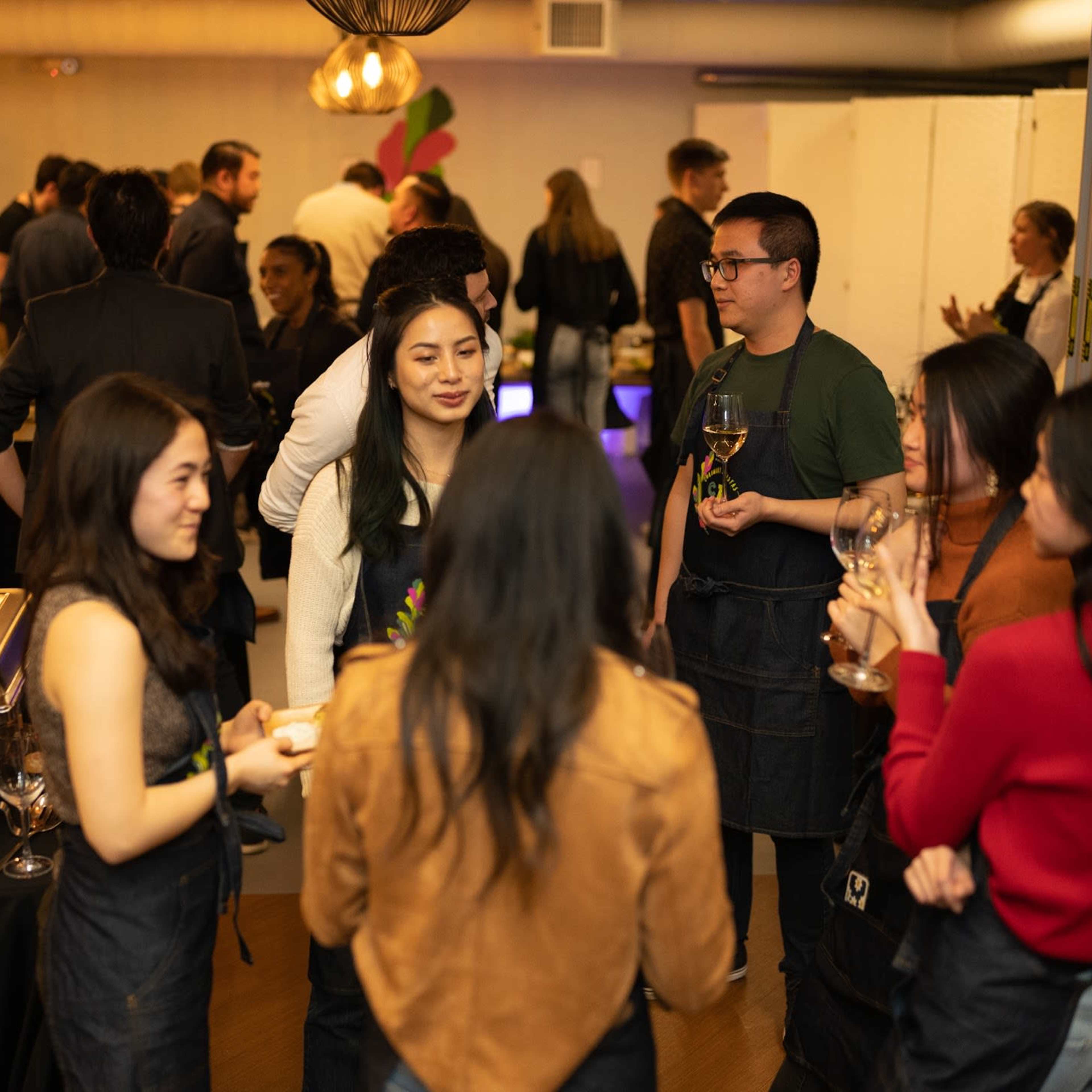 A group of people converses and mingles at a social event featuring food and drinks in a warmly lit venue.
