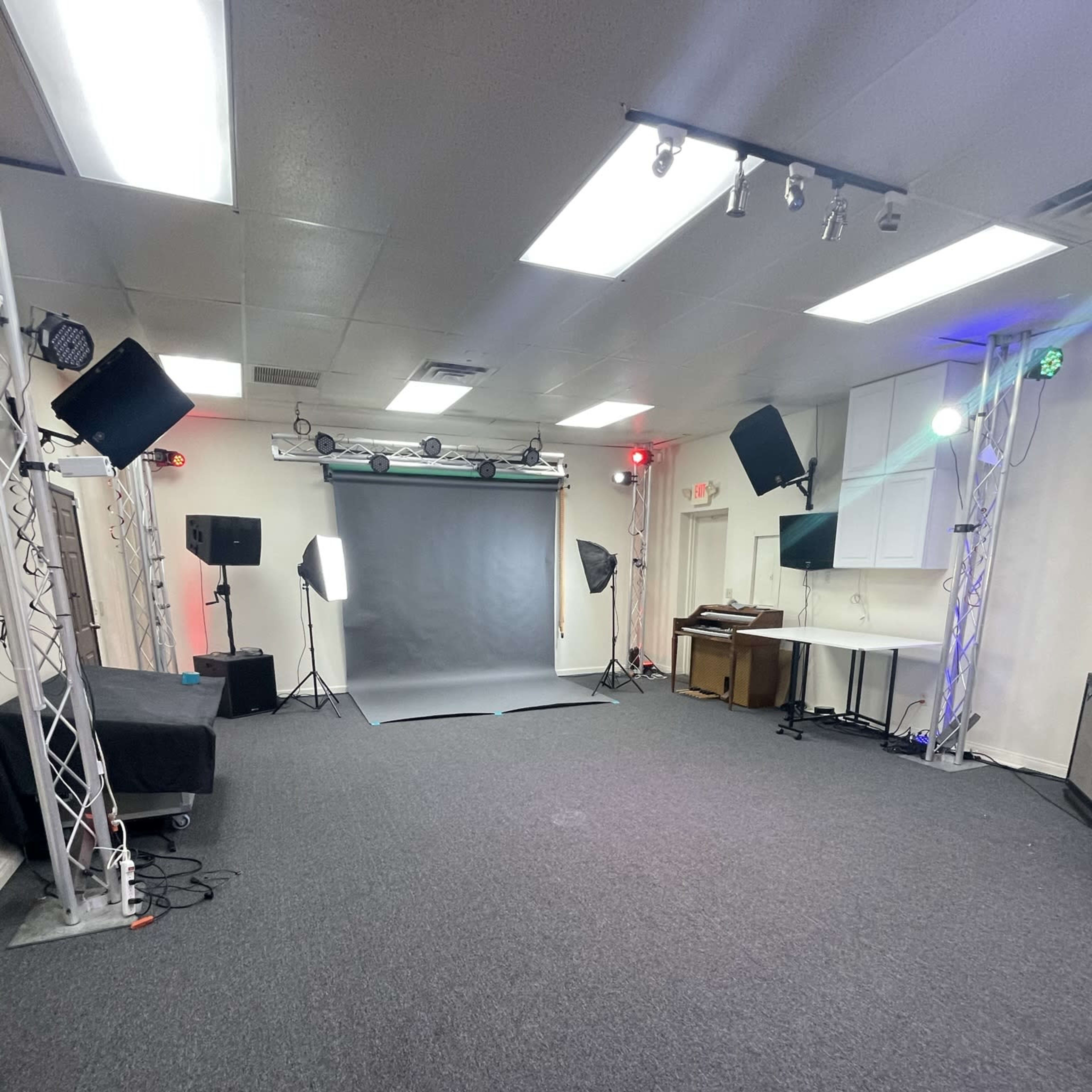 A well-lit studio space with a gray backdrop, studio lights, and sound equipment arranged on a carpeted floor.