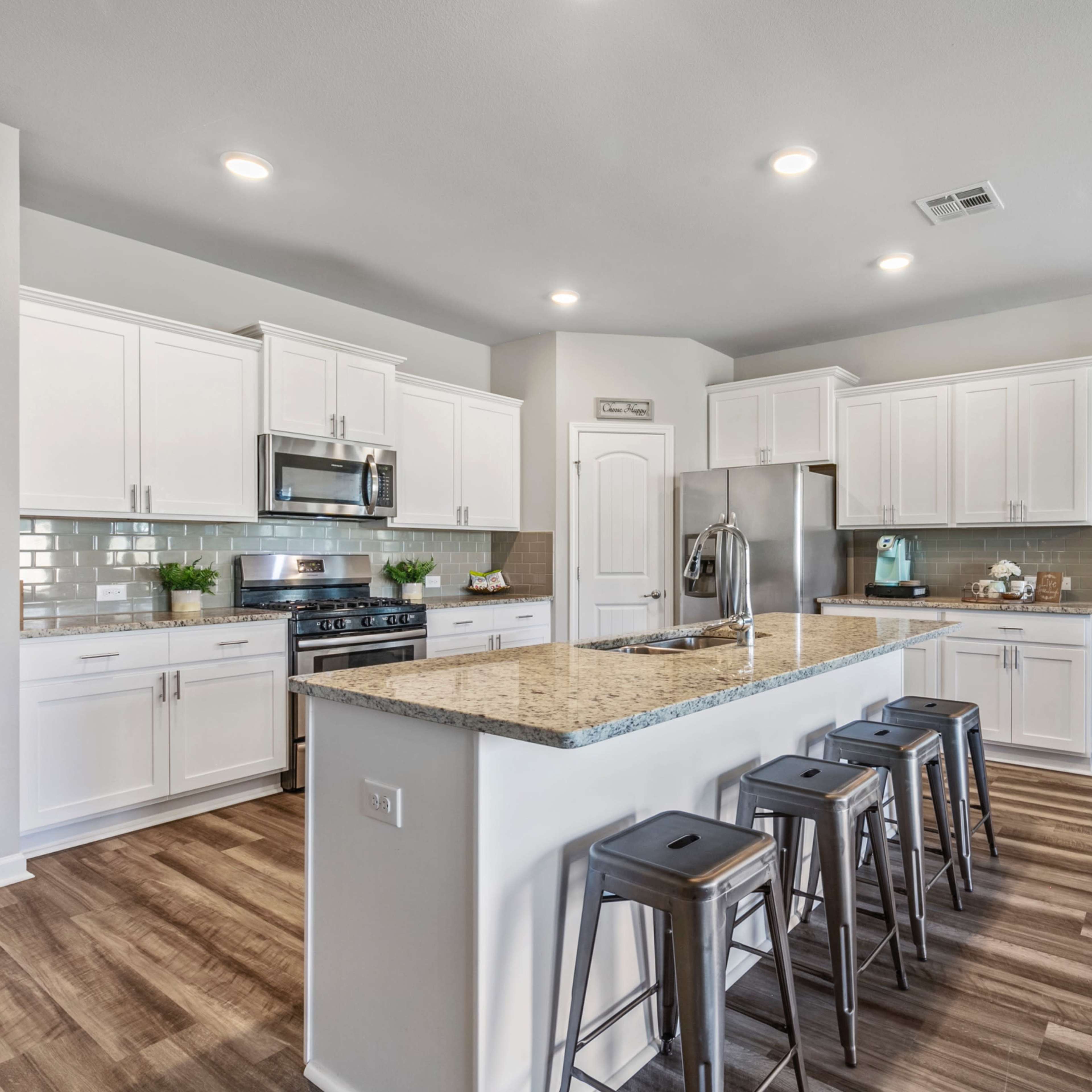 A modern kitchen features white cabinets, stainless steel appliances, a large island with seating, and wooden flooring.