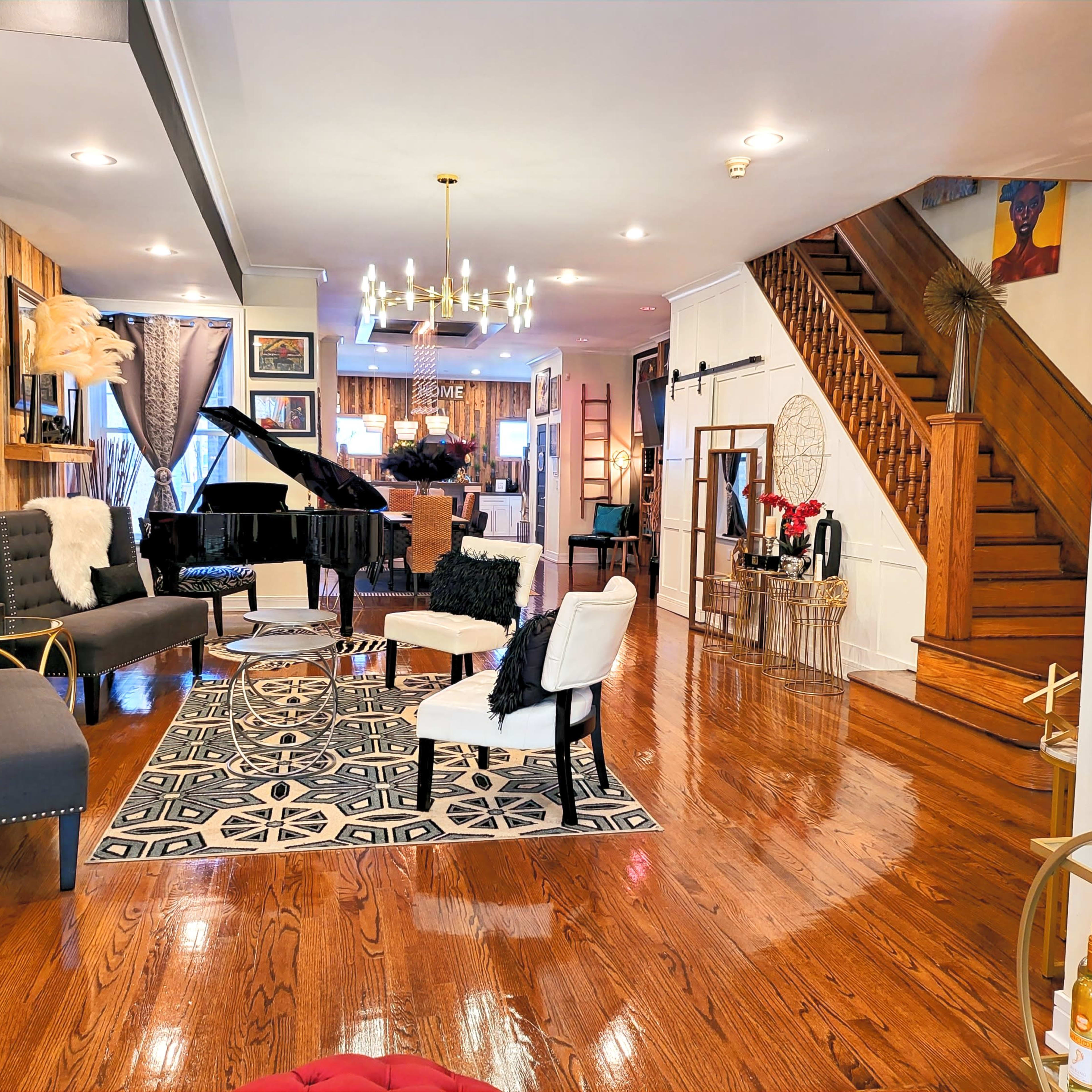 A stylish living room with hardwood floors, a grand piano, seating arrangements, and a staircase leading to an upper level.