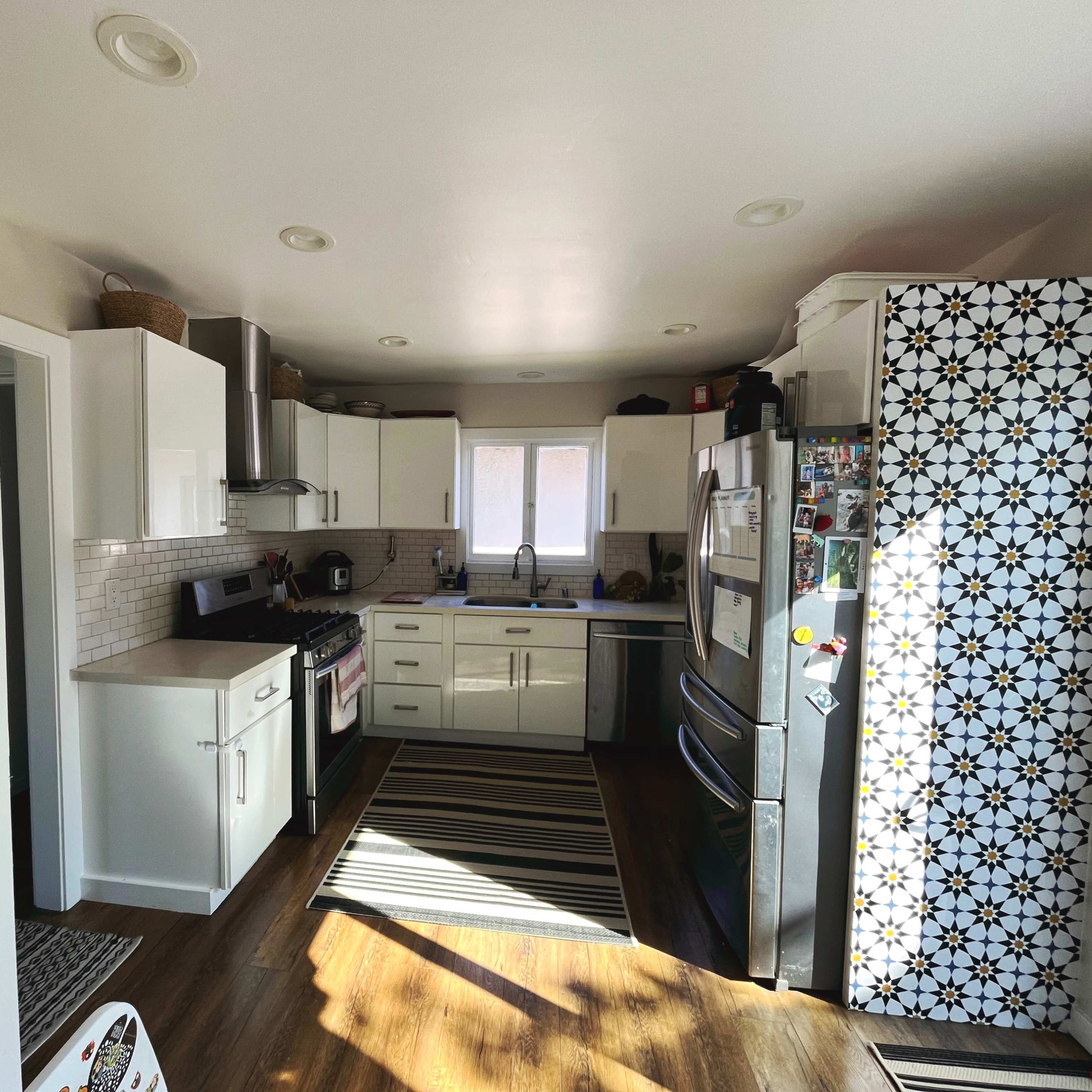 A bright kitchen features white cabinets, a stainless steel refrigerator, and a striped rug on the floor.