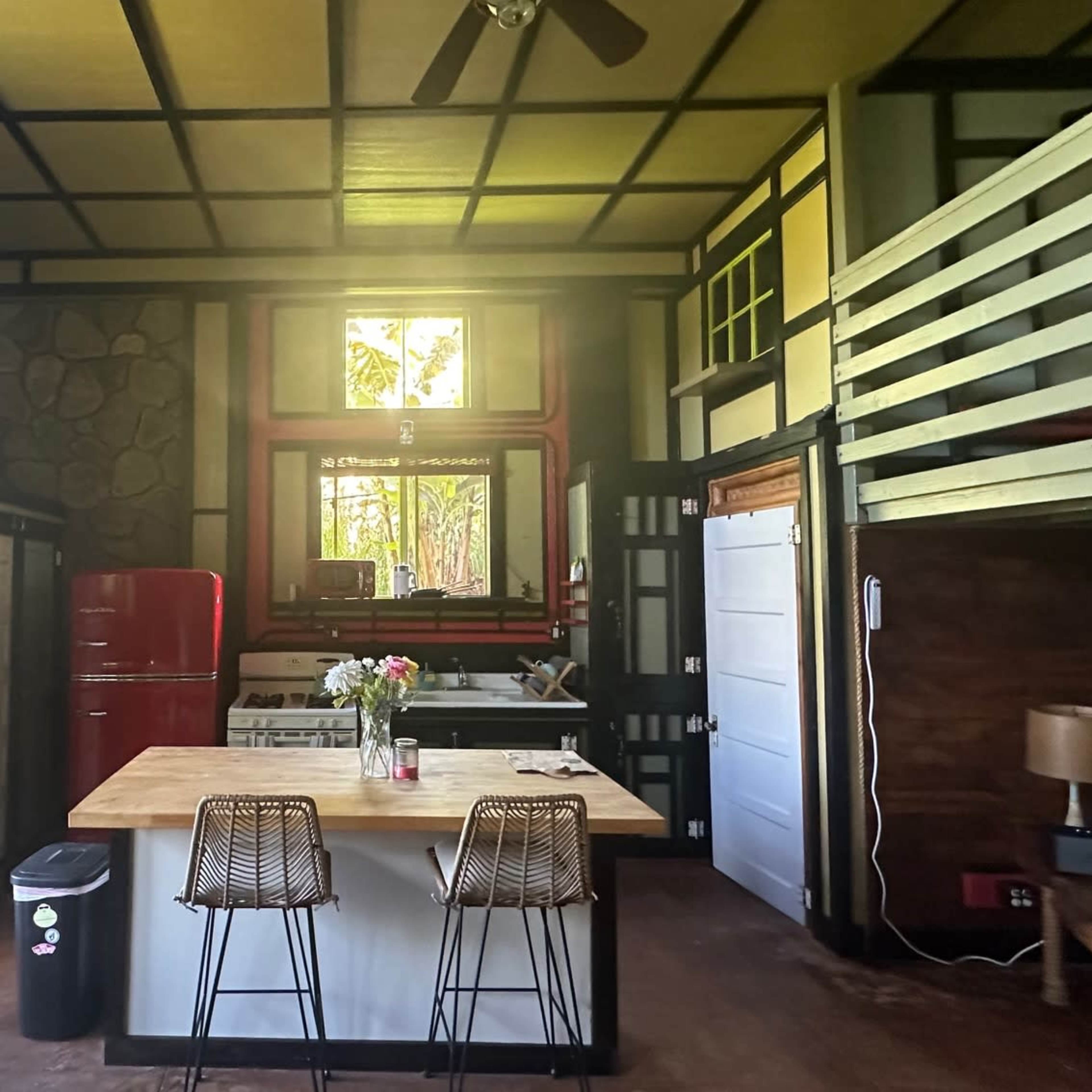 A spacious, modern kitchen and living area with a lofted sleeping area, featuring a red refrigerator and a large island with bar stools.