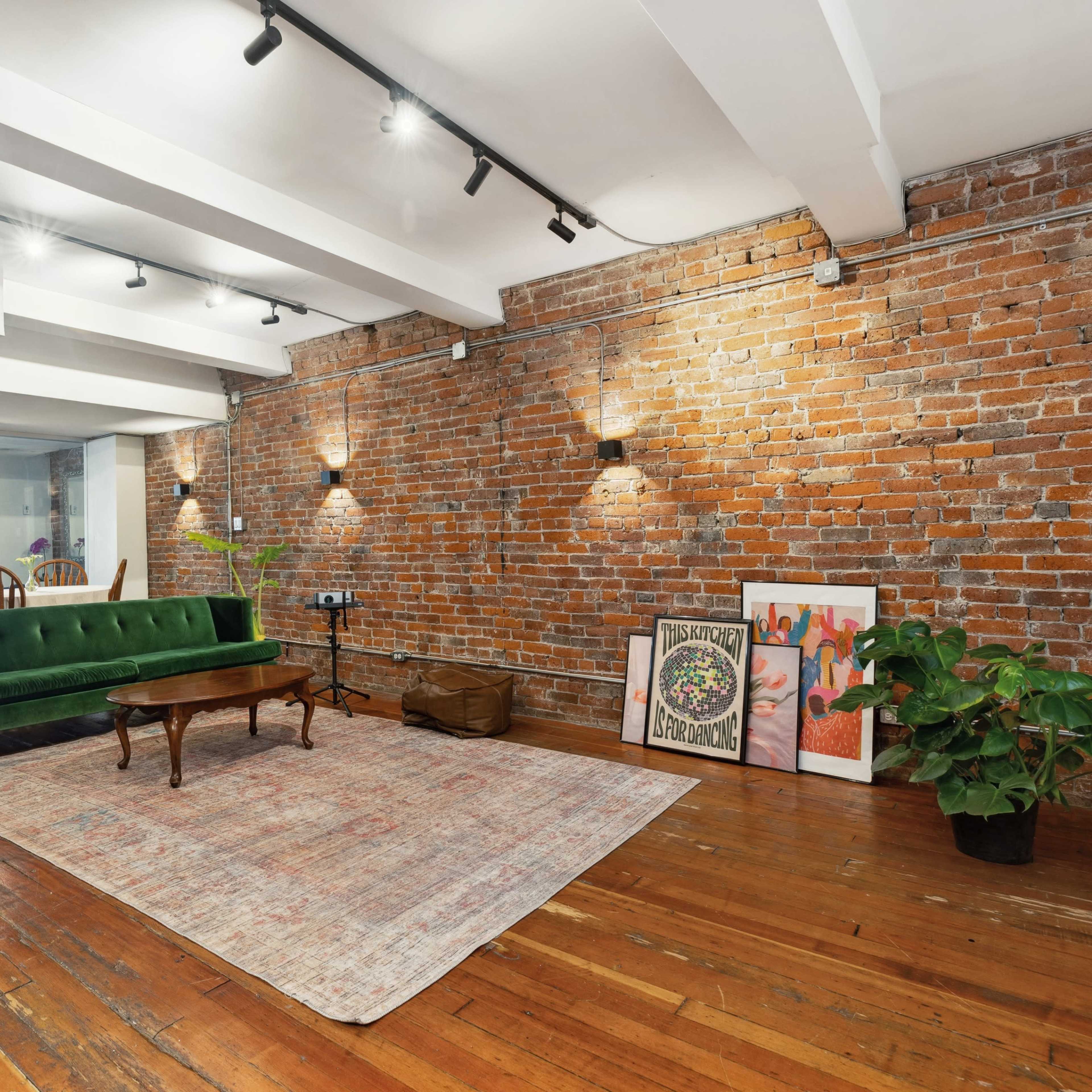 A spacious room with exposed brick walls, wooden floors, a green velvet sofa, a wooden coffee table, and decorative artwork on the floor.