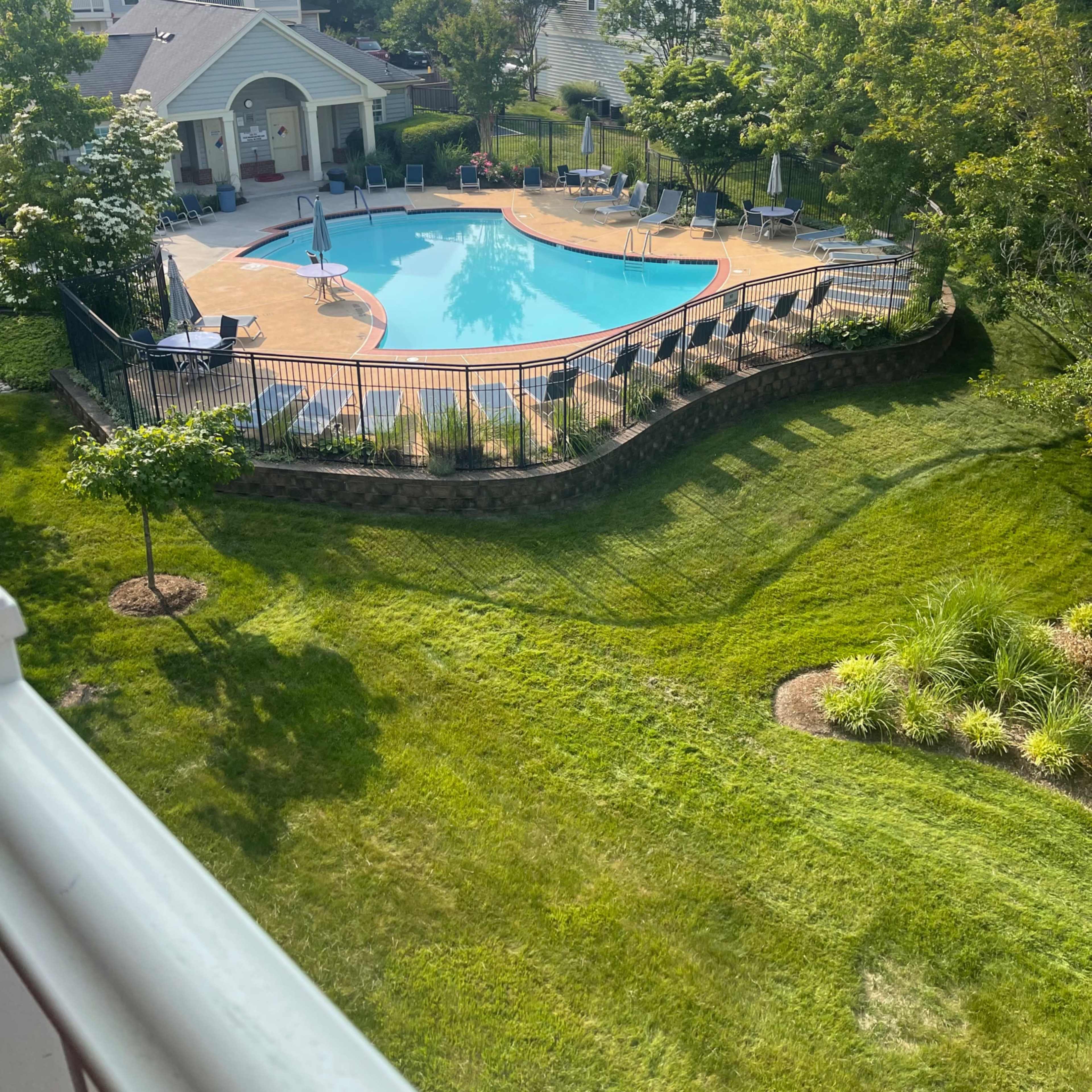 A landscaped outdoor area featuring a rectangular swimming pool surrounded by lounge chairs, a wooden deck, and neatly trimmed grass.