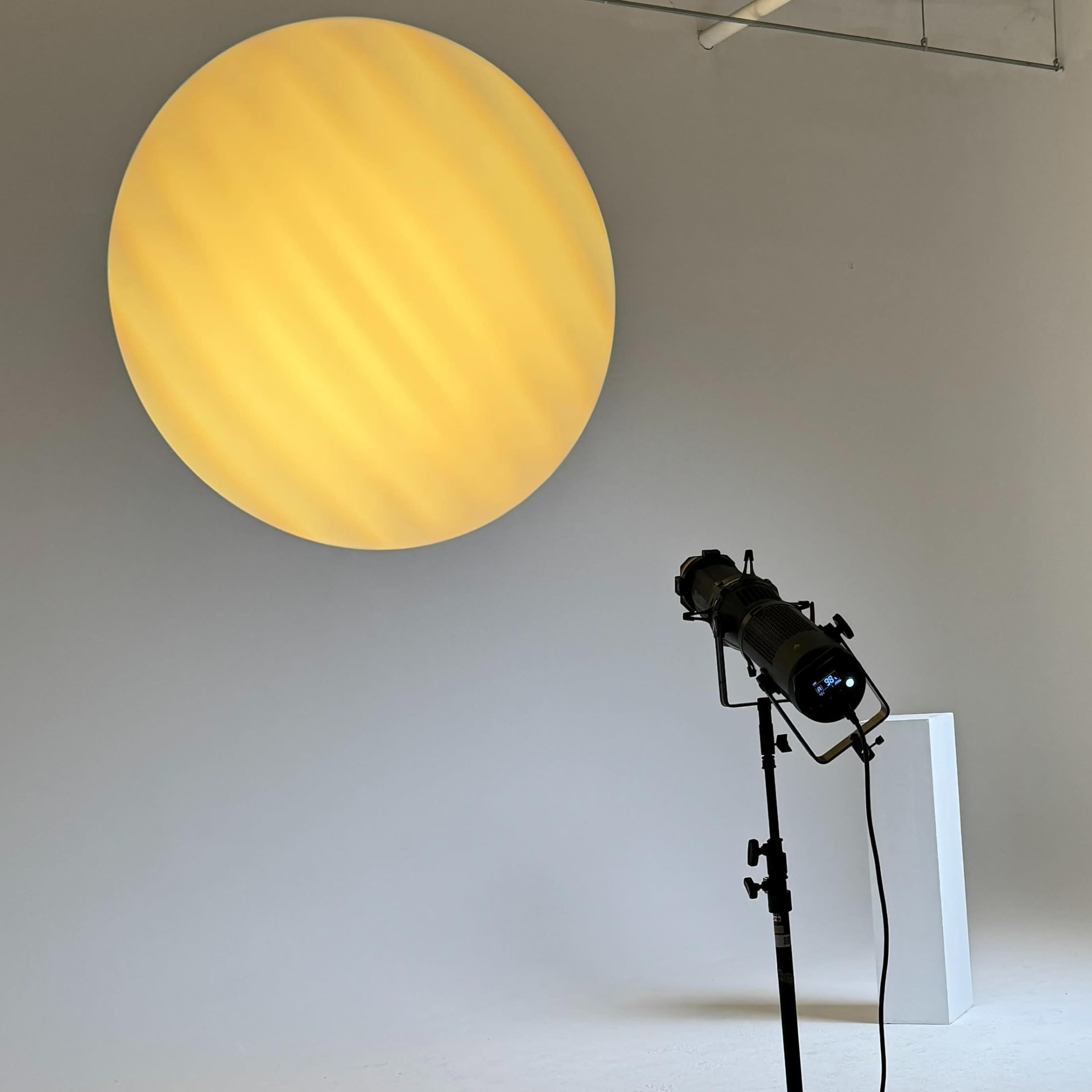 A photography studio with a large yellow circular backdrop and three lighting setups, including two softboxes and a spotlight.