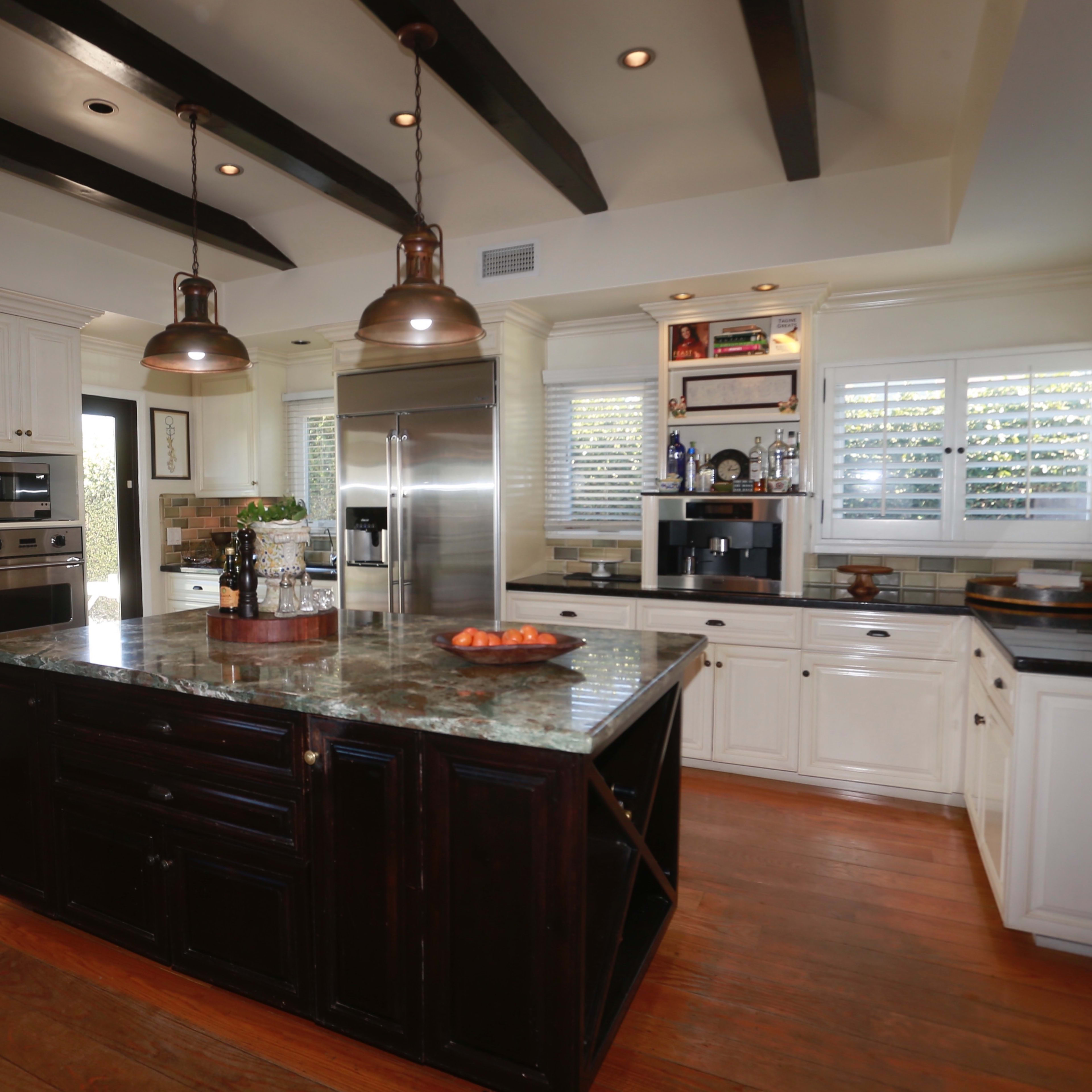 The kitchen features a central island with a dark wood base, stainless steel appliances, and white cabinetry with a tile backsplash.