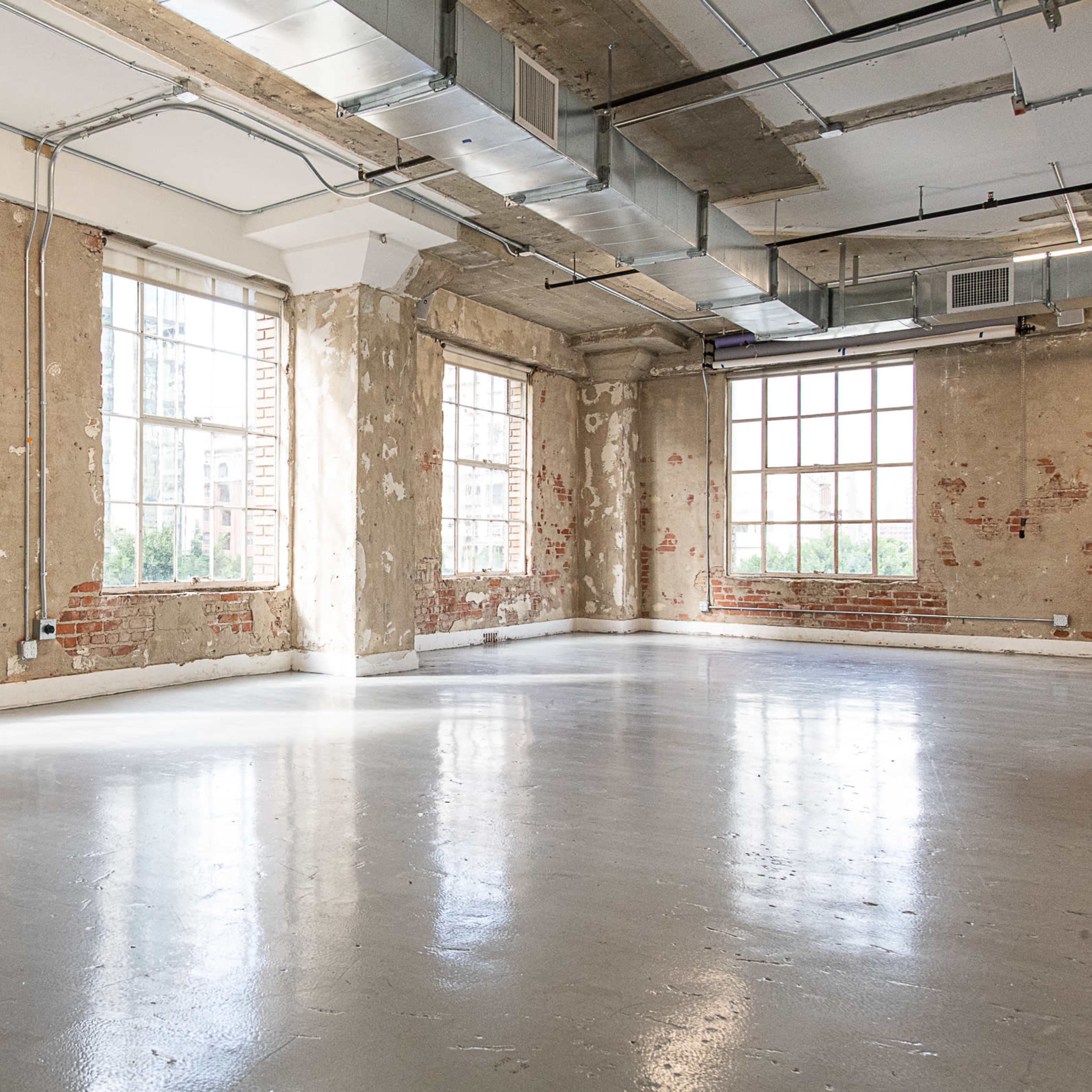 An empty industrial space with large windows and exposed brick walls.