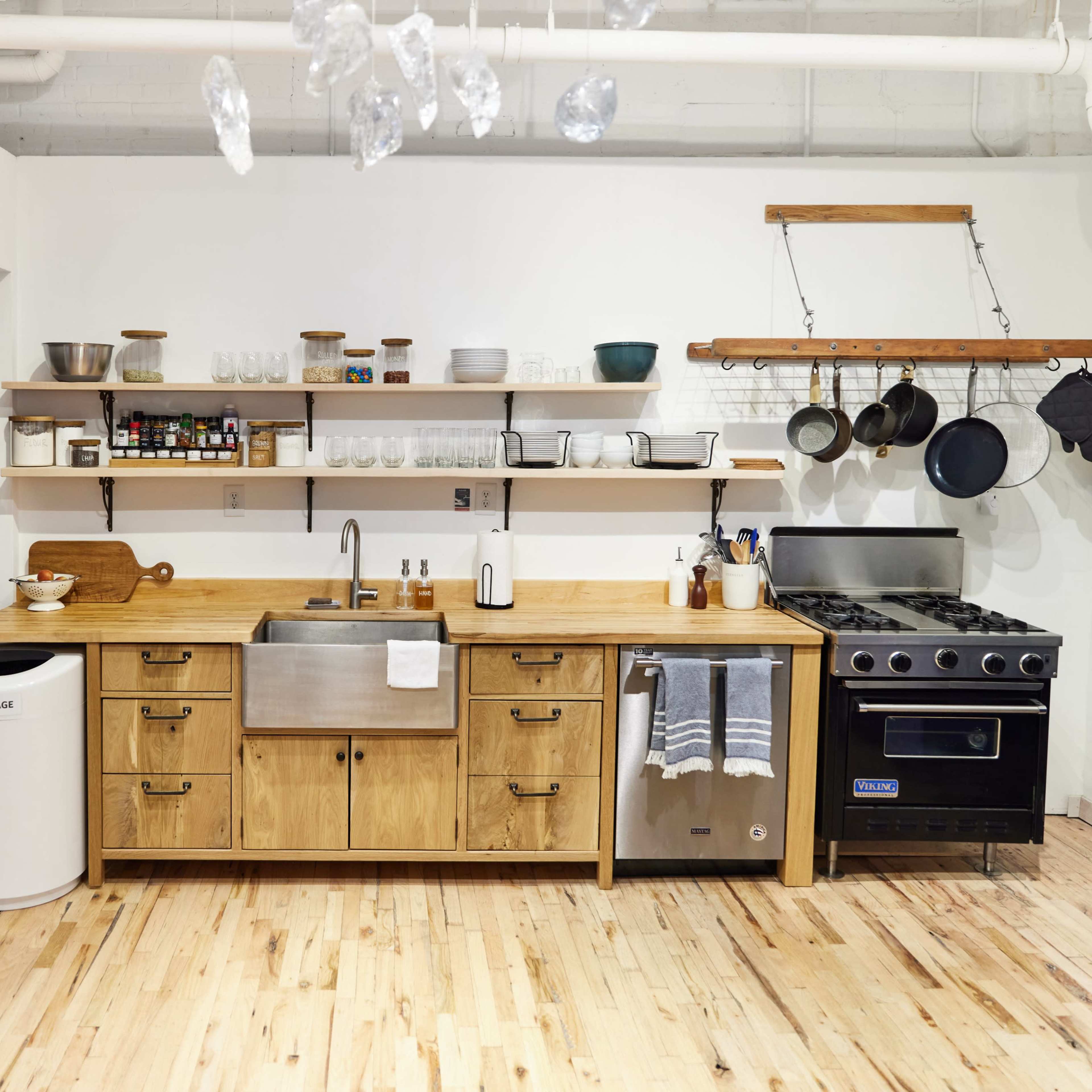 The kitchen features stainless steel appliances, a wooden countertop, open shelving with dishware, and hanging pots.