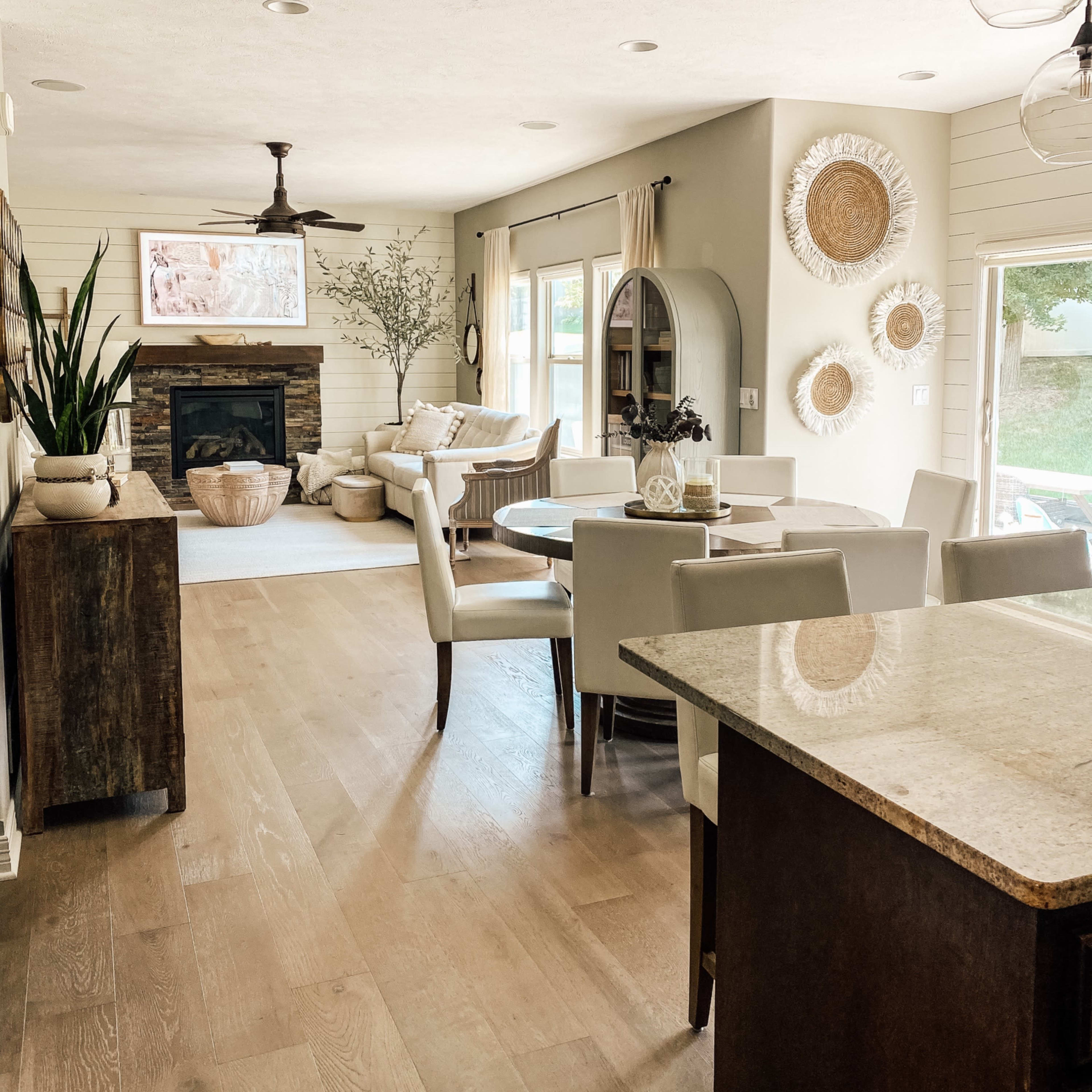 A light-filled living space features a dining area with a wooden table, a cozy seating area with a fireplace, and decorative wall accents.