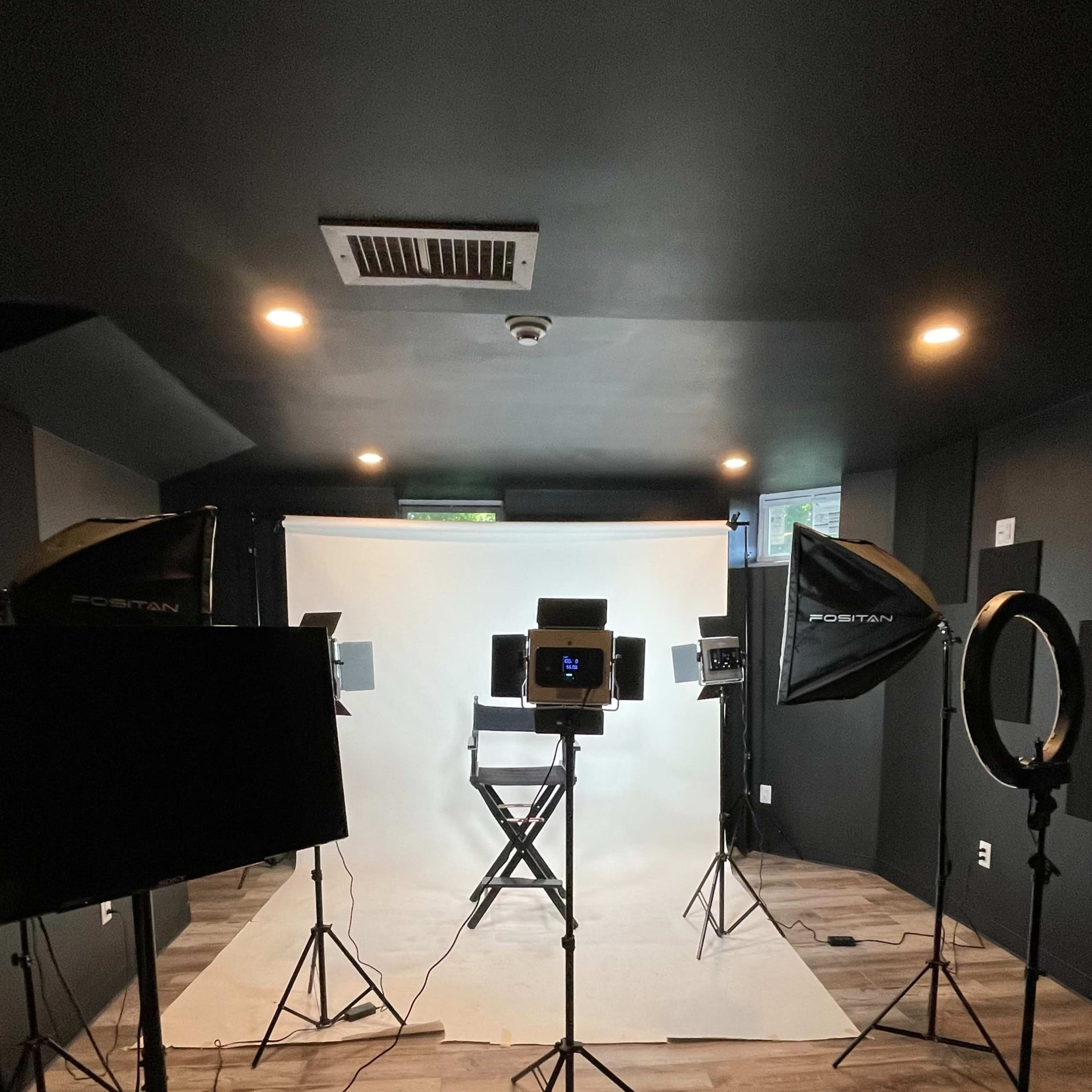 A photography studio set up with lighting equipment, a white backdrop, and a director's chair.