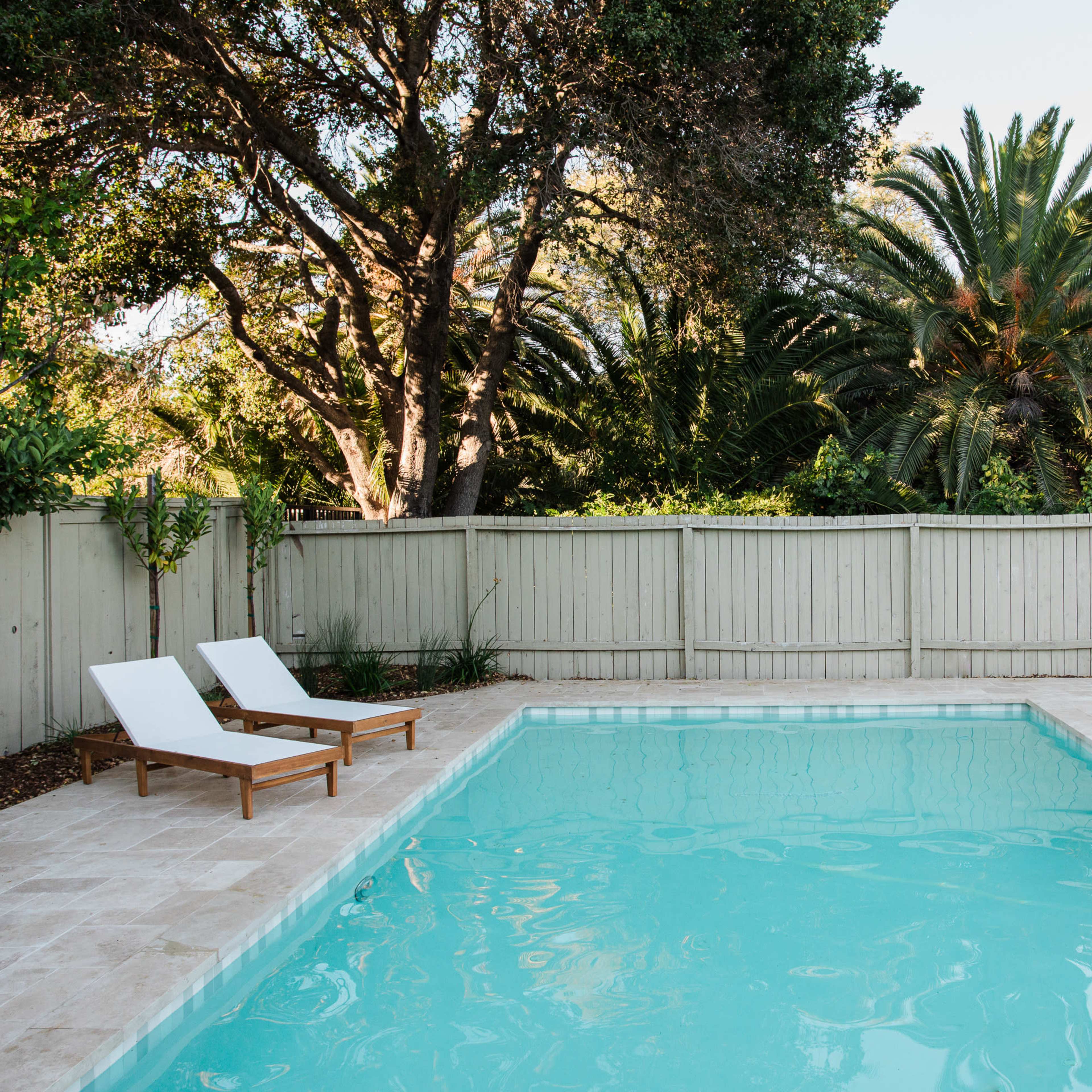 A well-maintained swimming pool surrounded by lounge chairs and lush greenery.