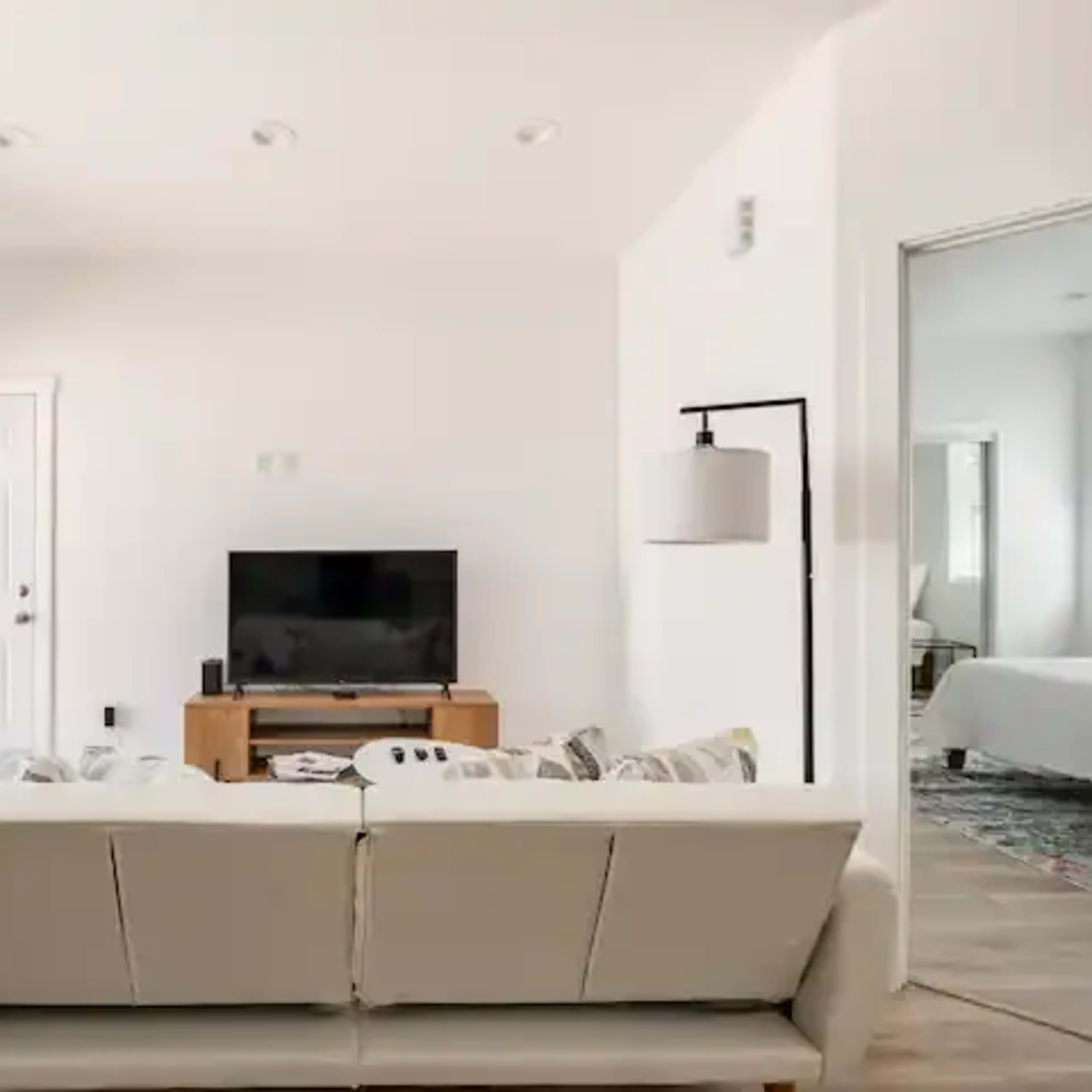 A modern living room features a beige sofa facing a television, with a door leading outside and a light fixture beside it.