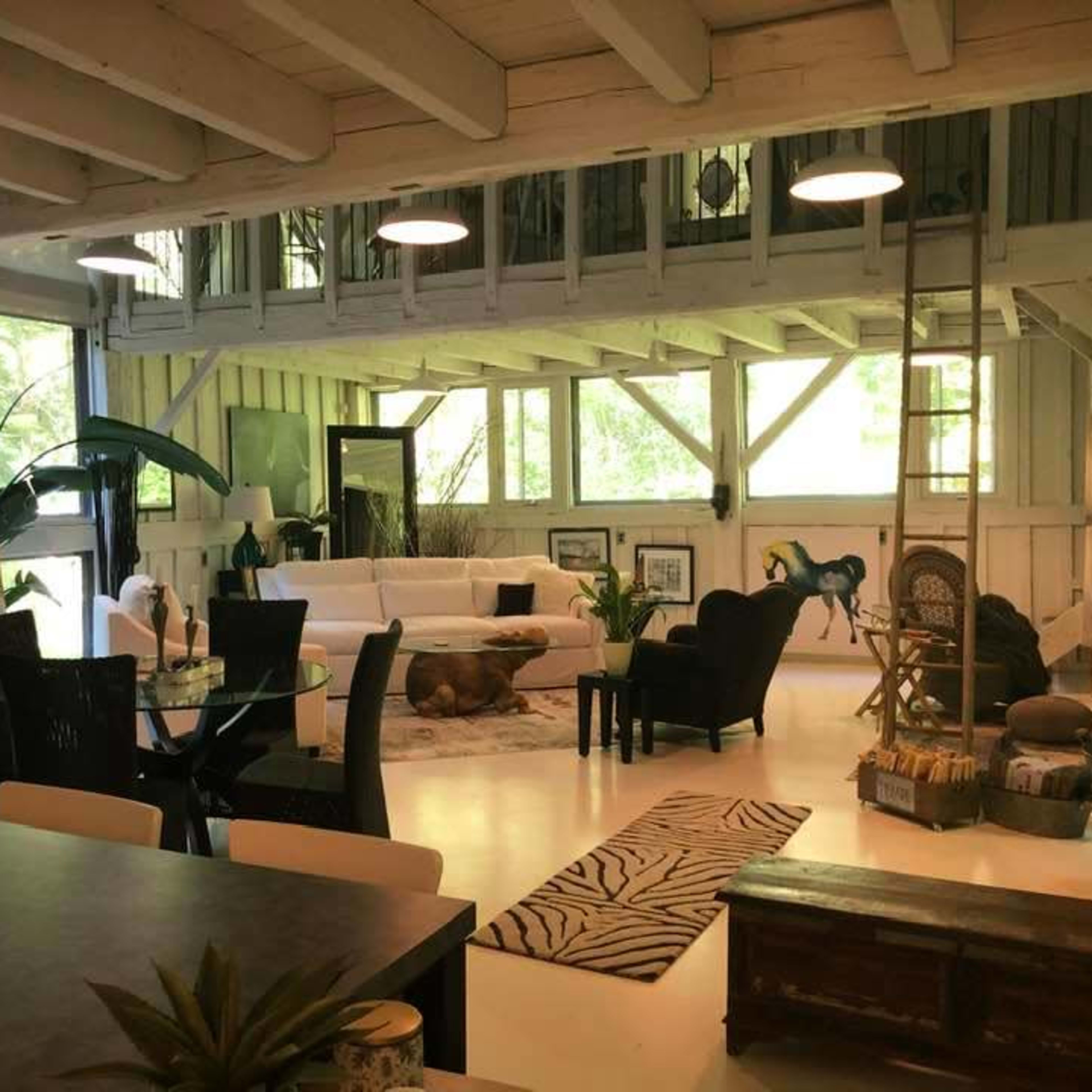 A well-lit, open-concept living space featuring a white sectional sofa, a dining area with a glass table, and large windows overlooking a green landscape.