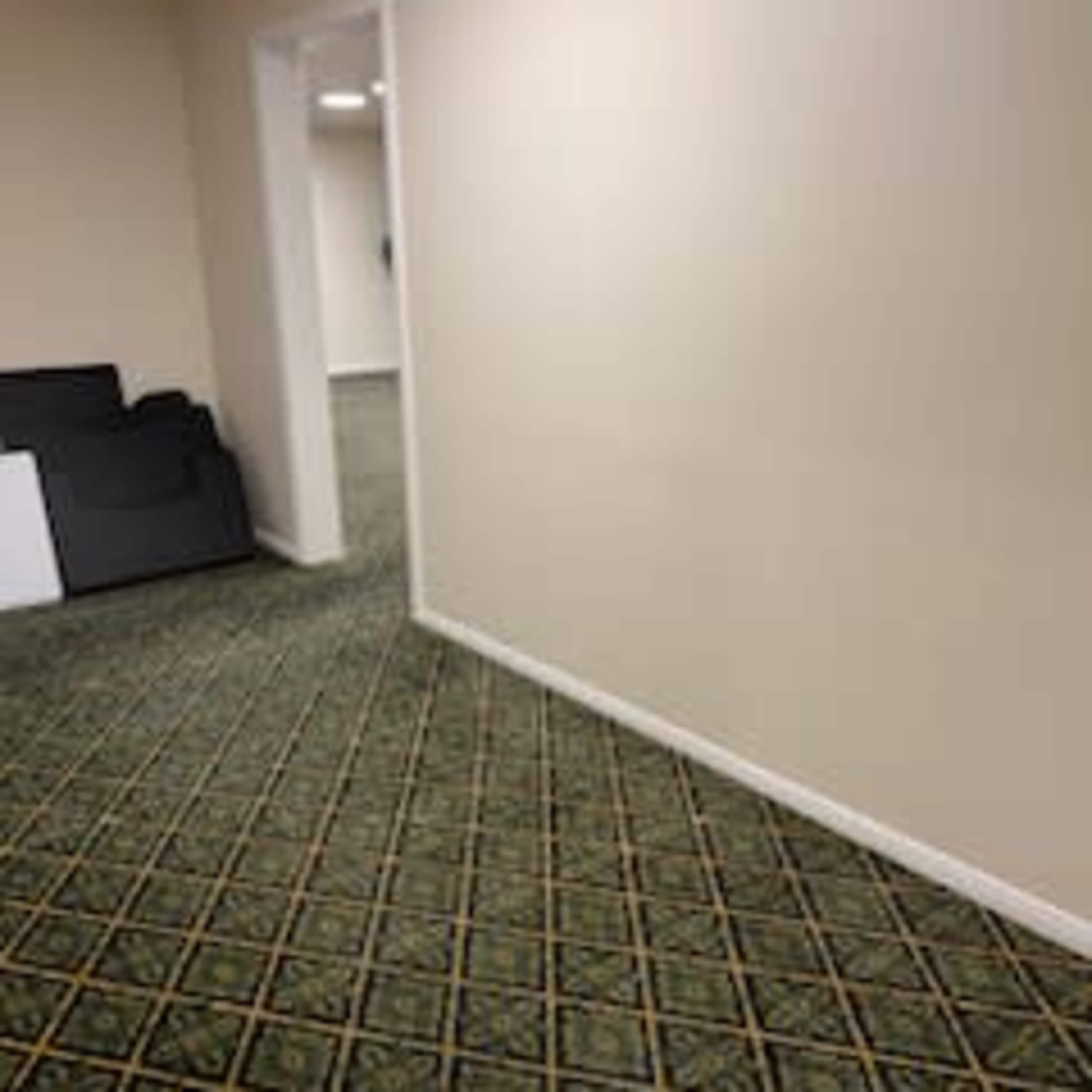 A hallway with a patterned carpet leads towards an open door, adjacent to a couch on the left.