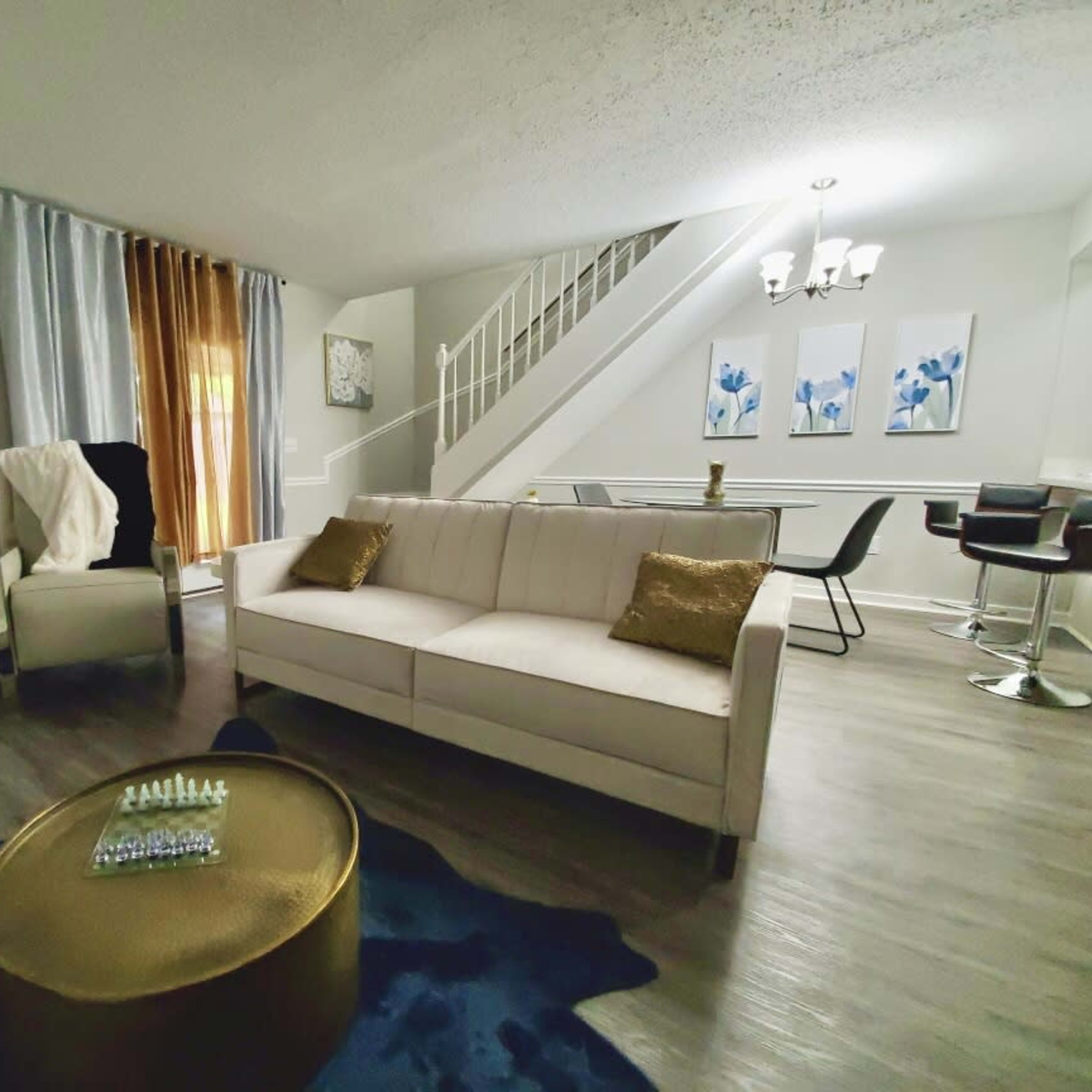 A modern living room features a beige sofa, a gold coffee table, and a staircase in the background.