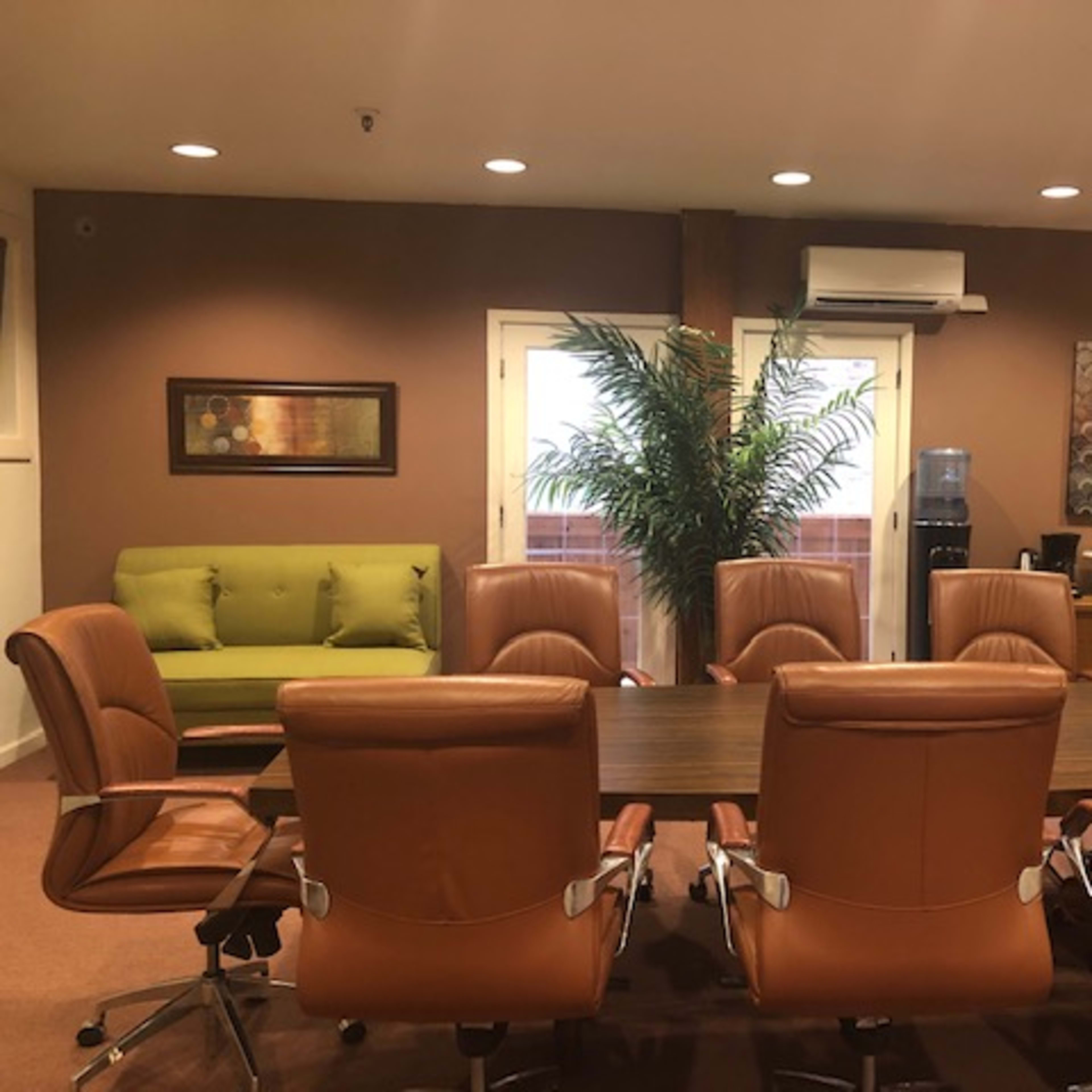 A conference room with a long wooden table surrounded by eight brown leather chairs and a green sofa against the wall.